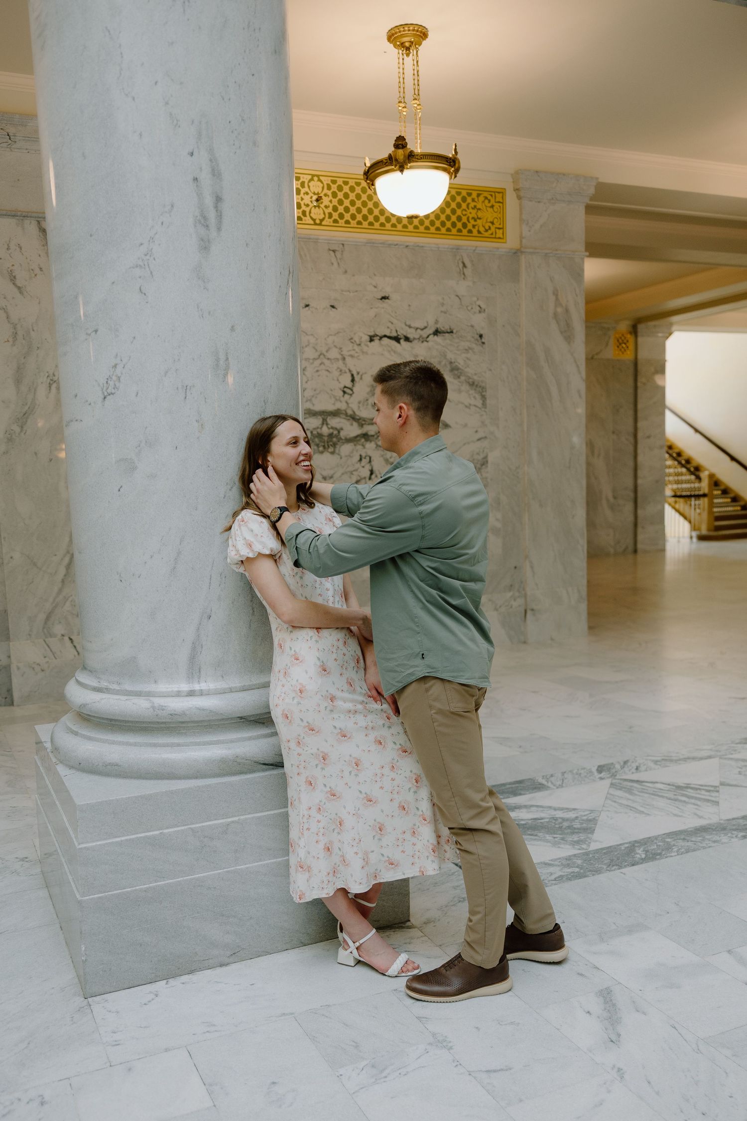 Young couple sharing an intimate moment leaning against a marble column in an ornate building.