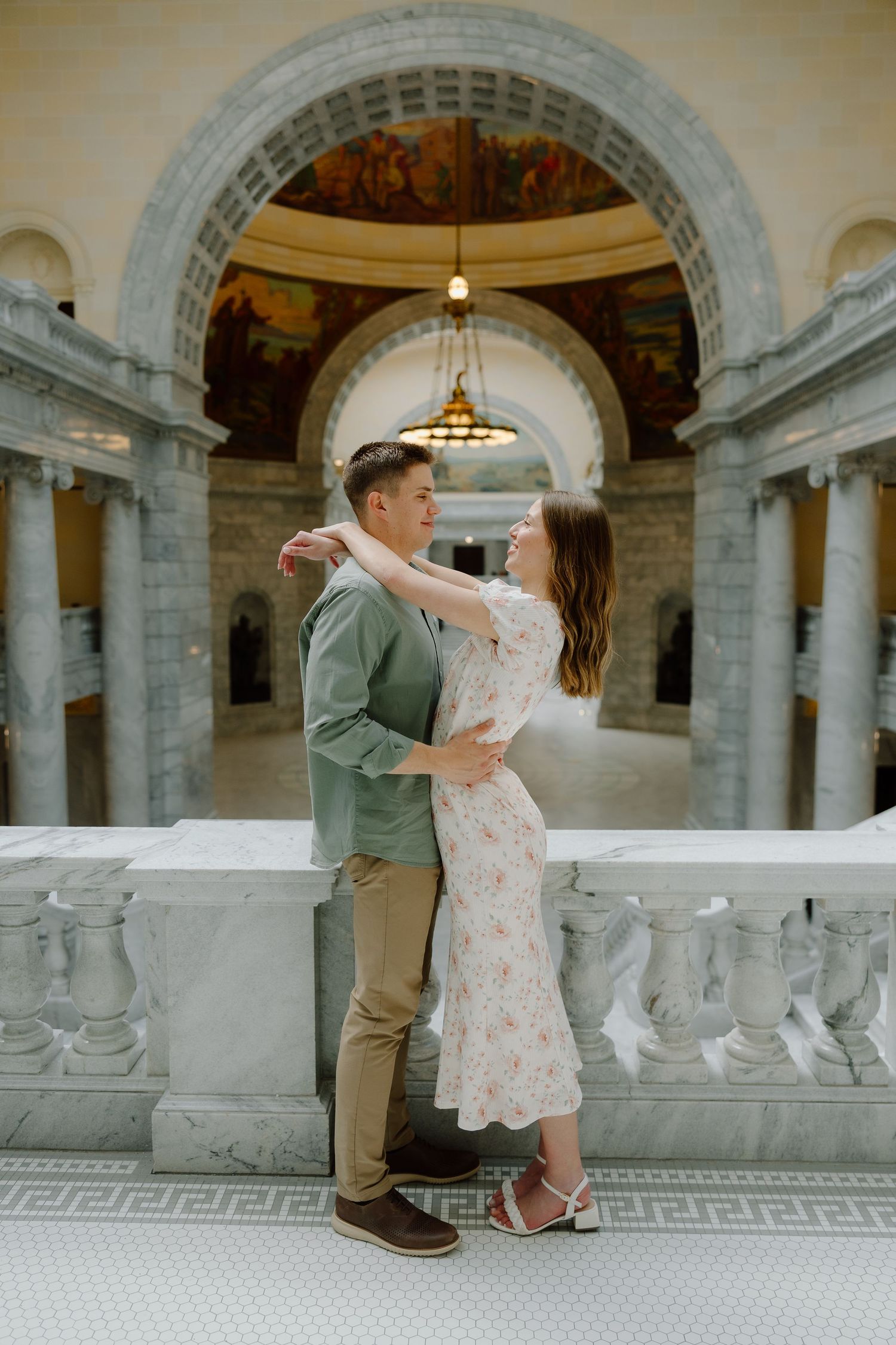 Couple embracing and dancing in elegant marble rotunda with ornate arched ceilings and classical architecture.