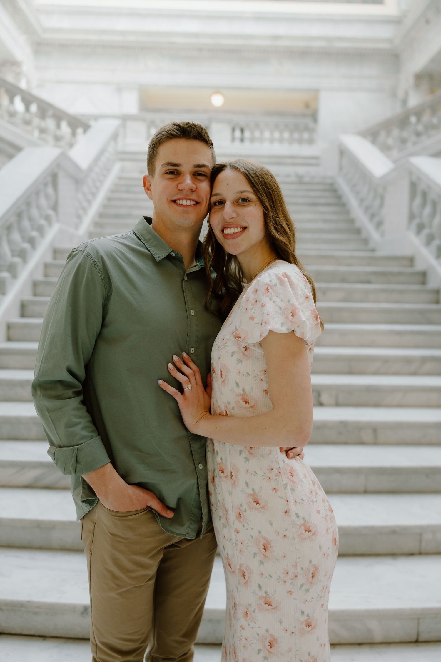 Smiling couple posing together on marble staircase, man in green shirt and woman in floral dress.