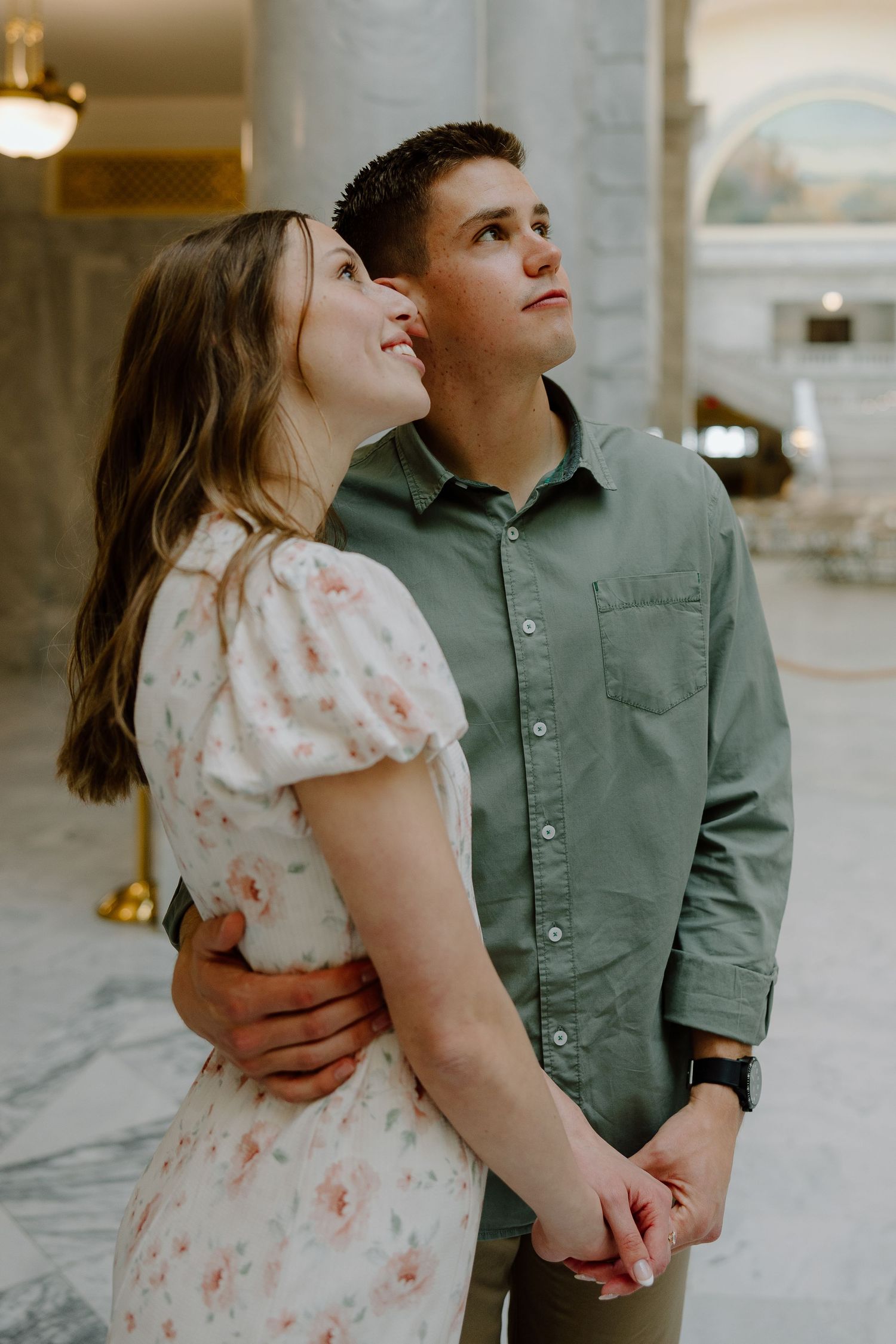 A loving couple embraces and gazes upward together inside a grand marble-columned rotunda.