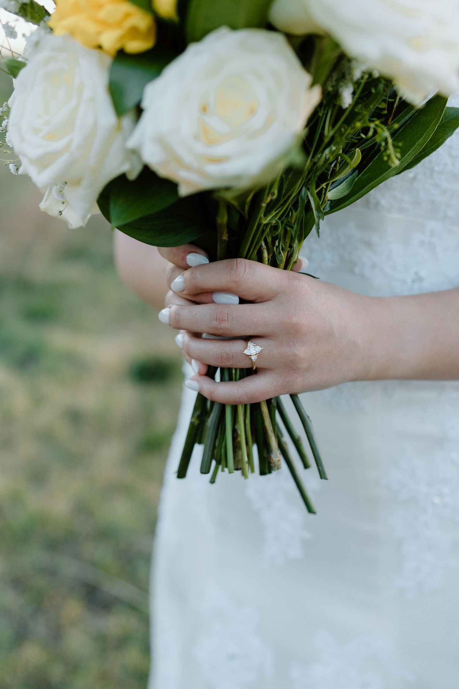 Close-up of bride holding white rose wedding bouquet showcasing elegant diamond engagement ring.