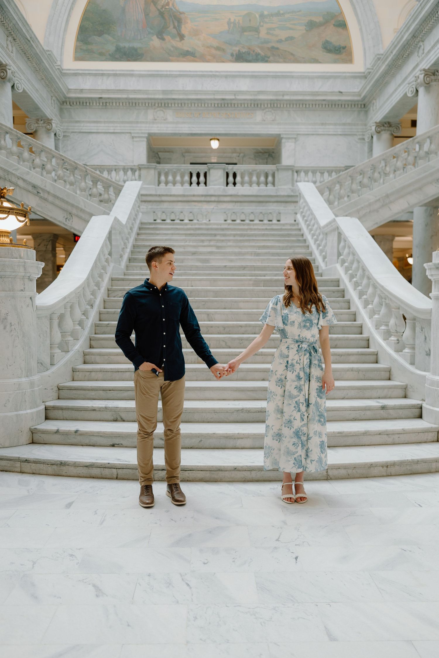 Couple holding hands in front of grand marble staircase inside a classical government building rotunda.
