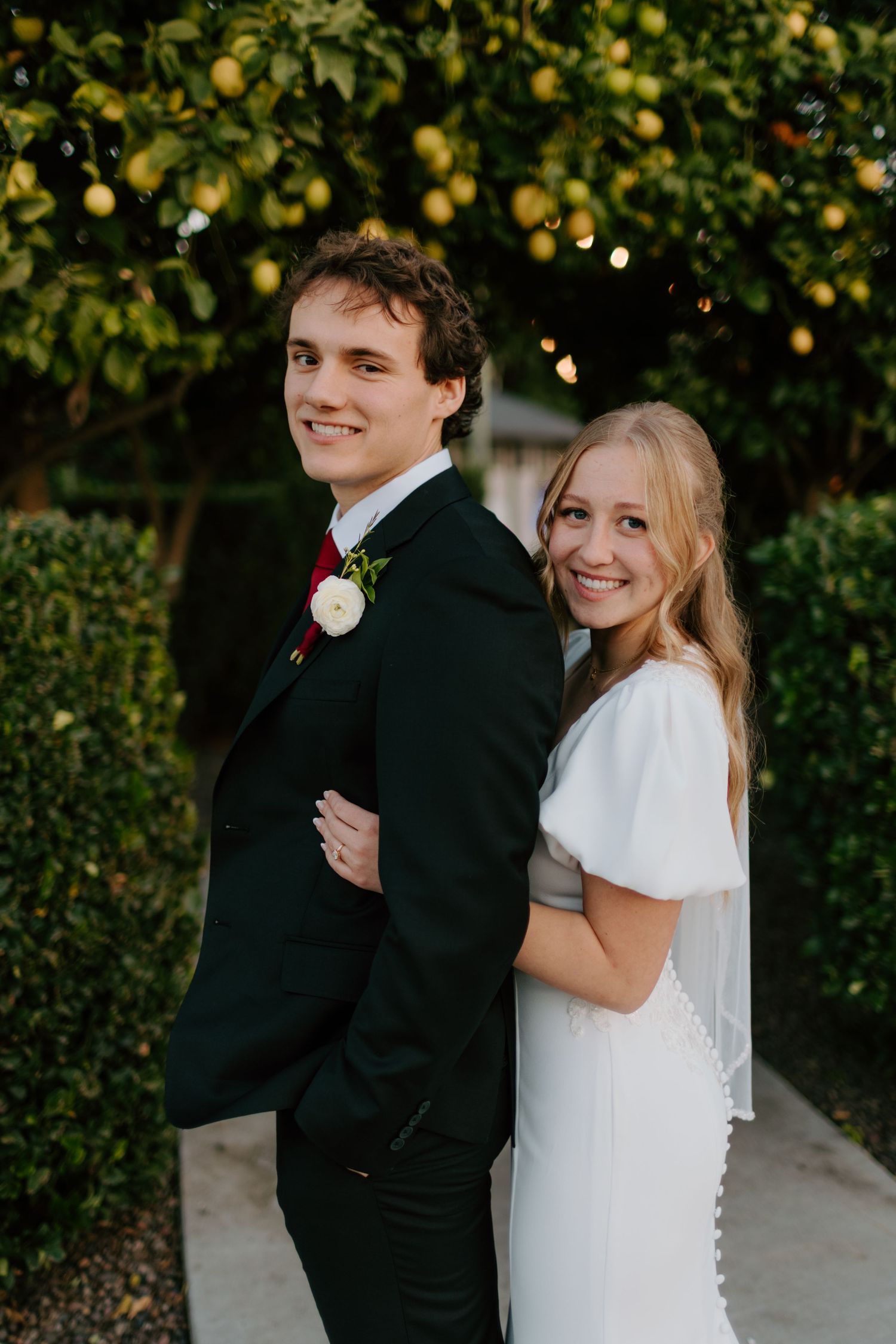 Smiling bride and groom stand back-to-back under string lights and a lemon tree at their wedding.