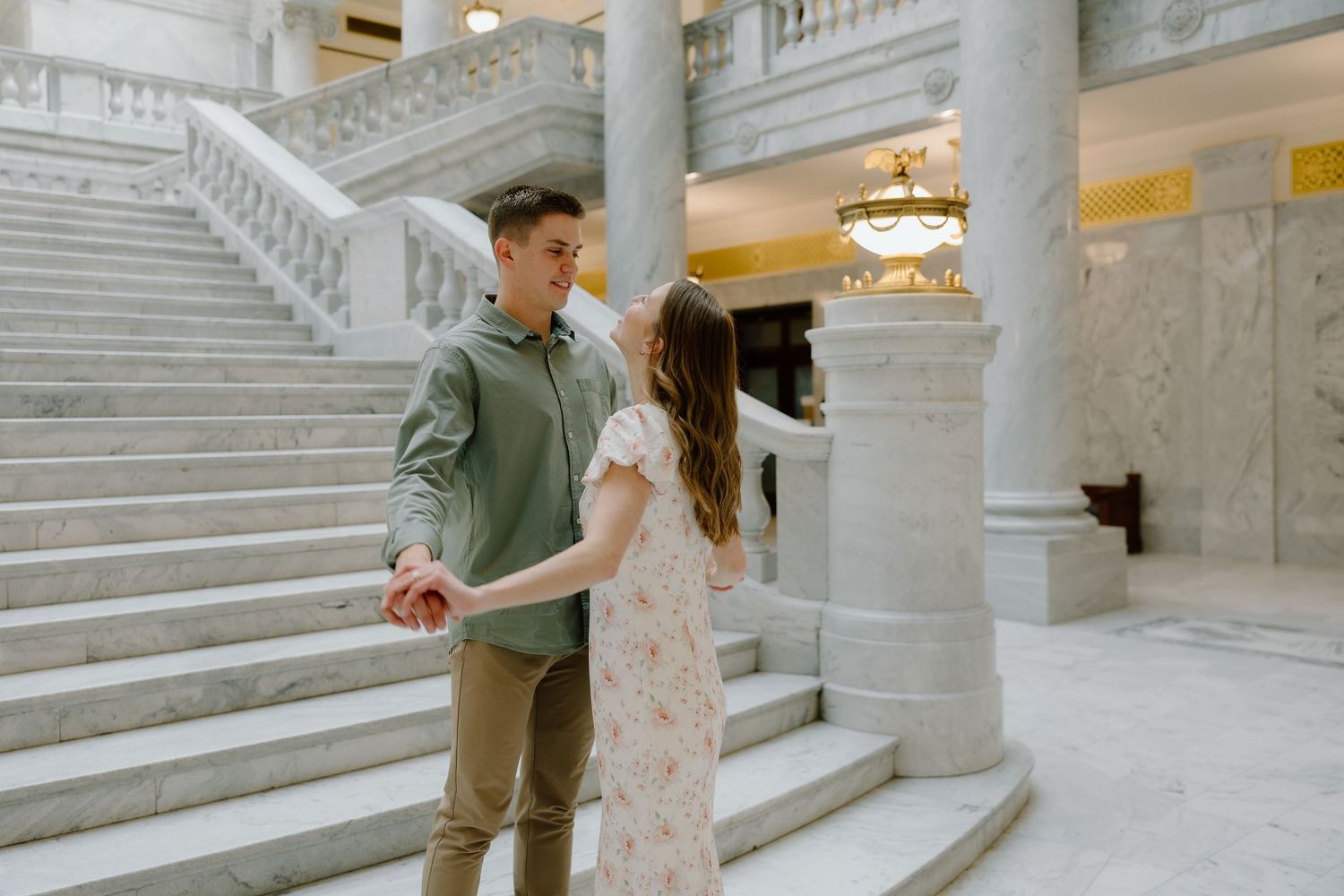 Couple holding hands and dancing near marble staircase in elegant building interior.