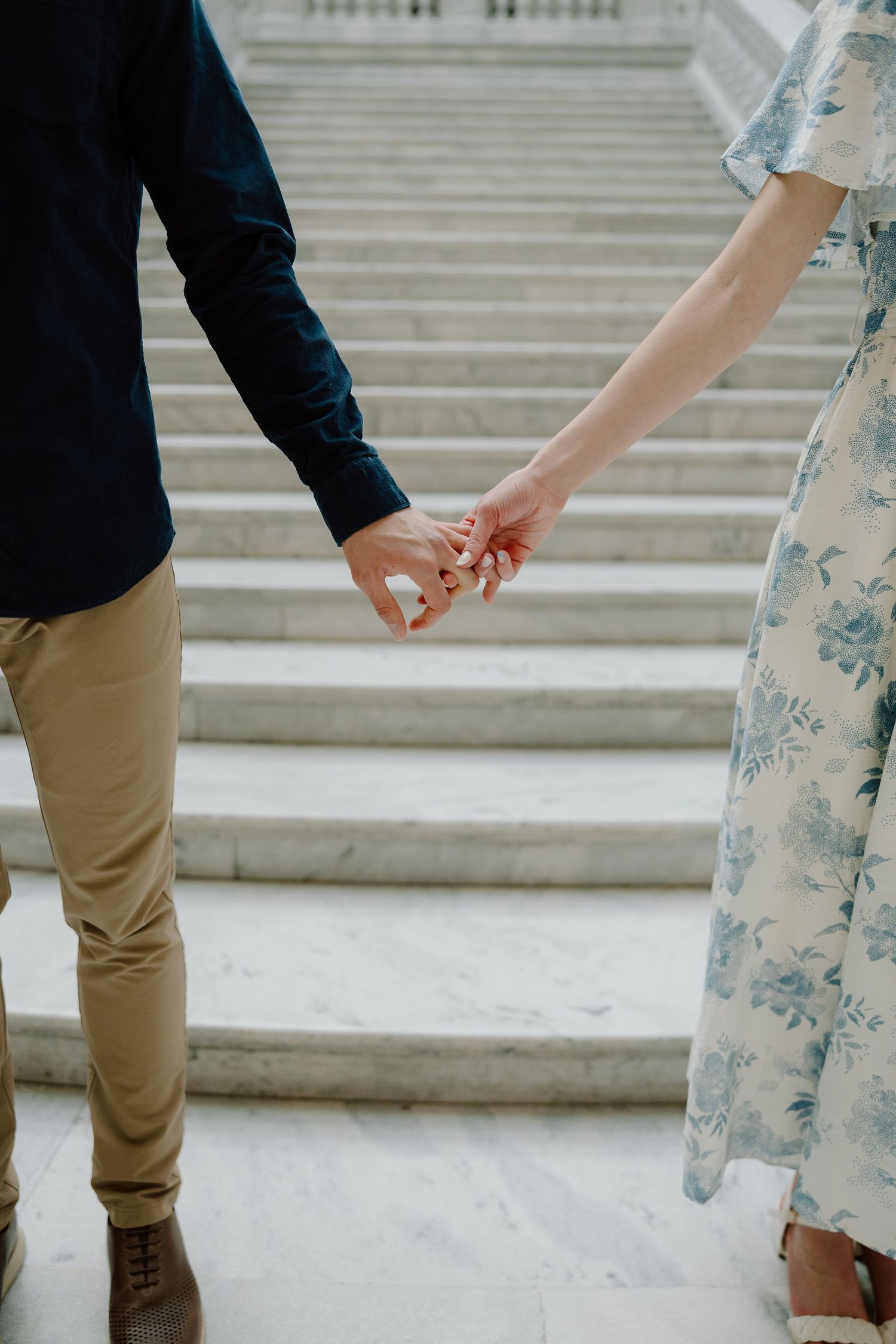 Couple holding hands on marble steps, man in navy shirt and khakis, woman in floral blue dress.