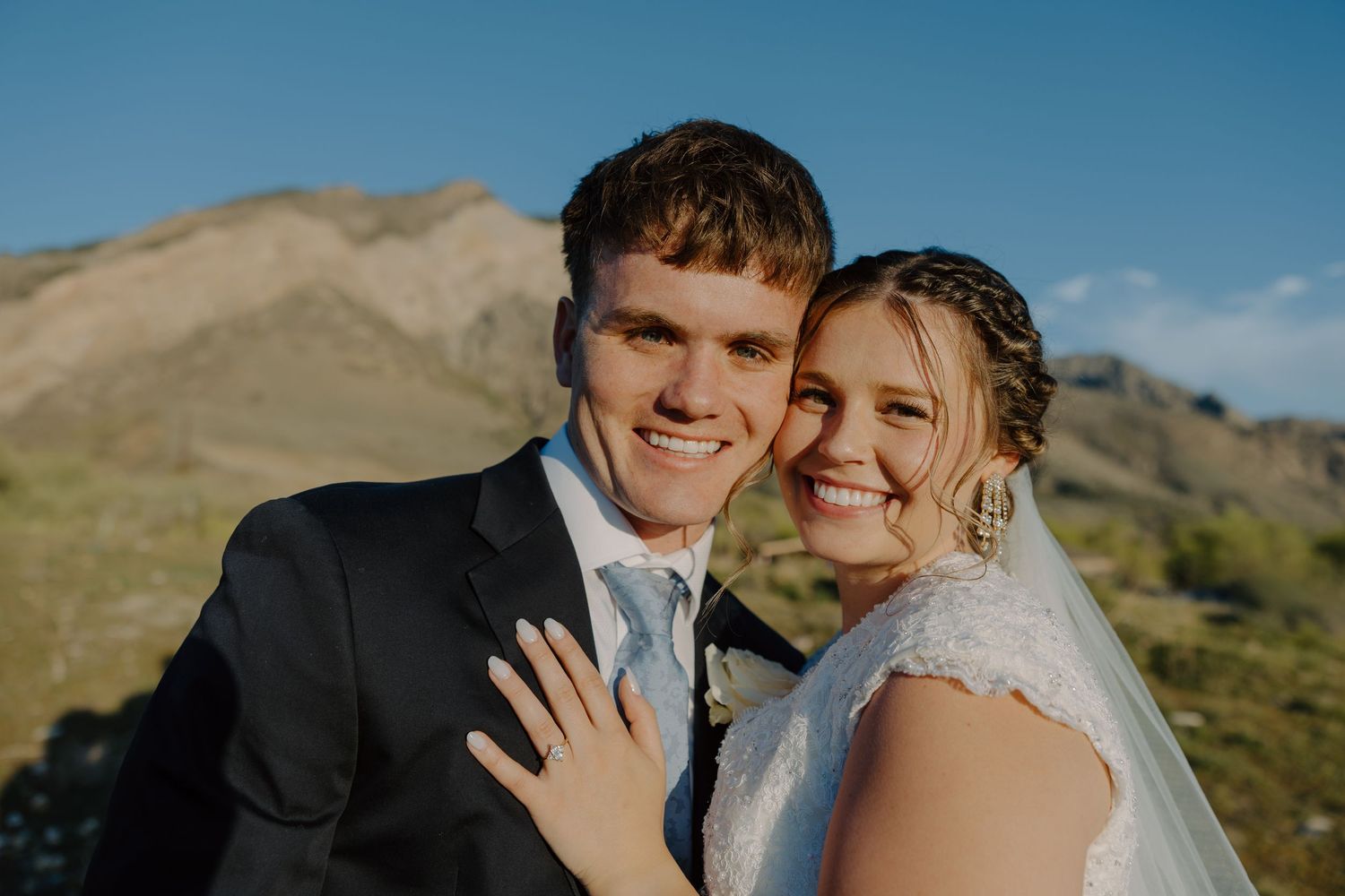 Happy newlywed couple smiling closely together with mountain backdrop, bride showing wedding ring.