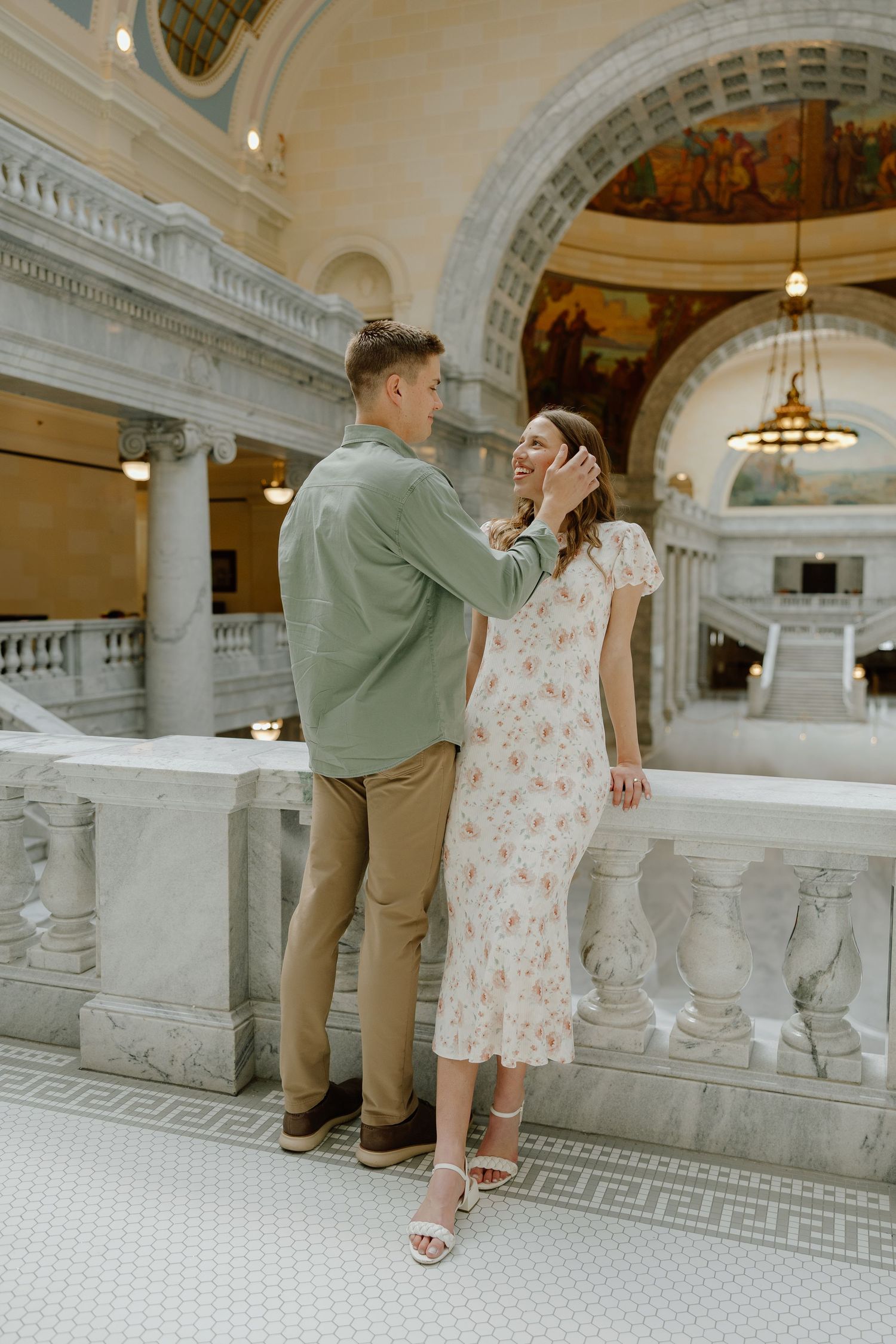 Romantic couple sharing a tender moment on a balcony inside a grand ornate capitol building.