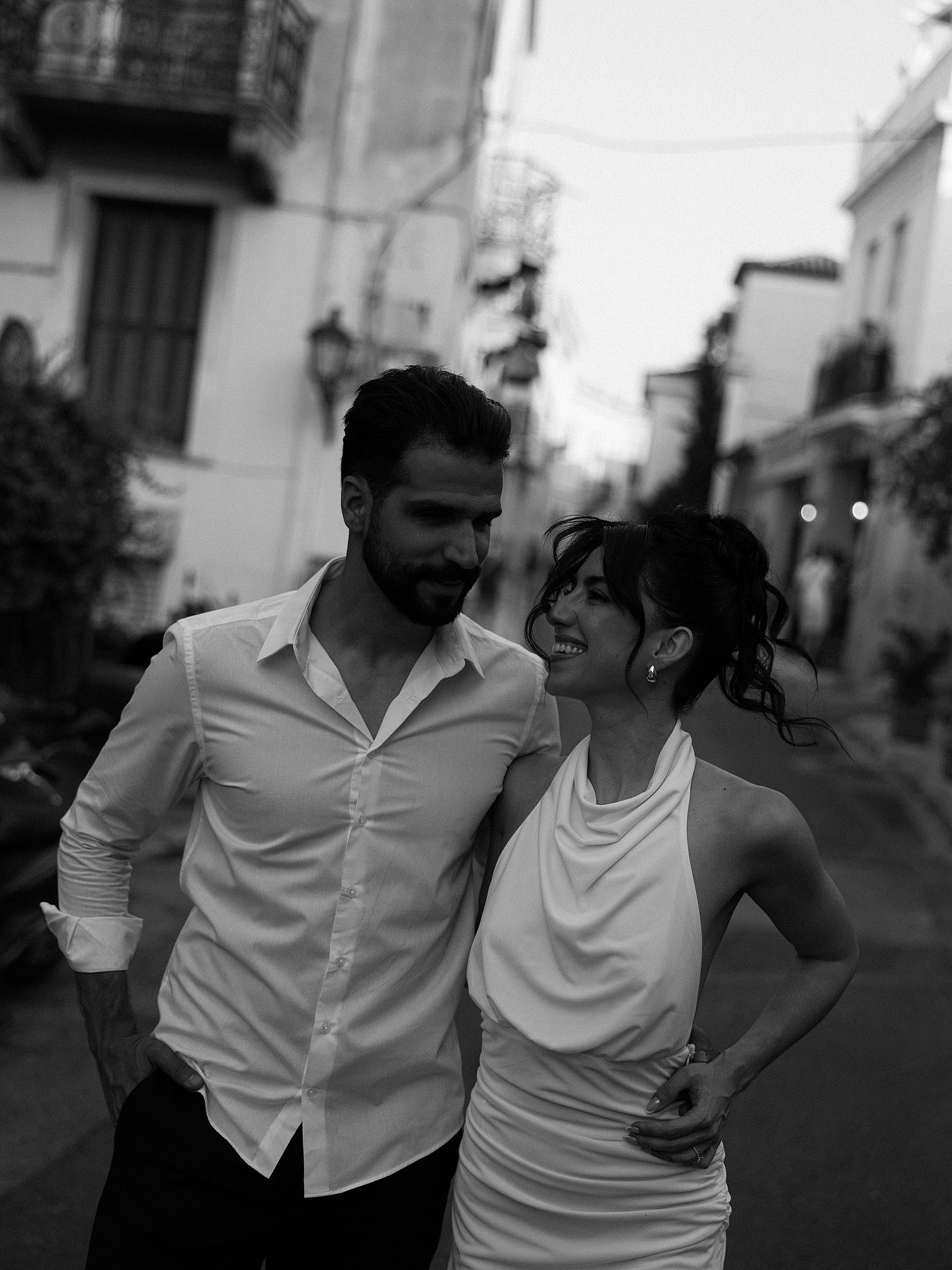 A couple in white clothing shares an intimate moment while dancing together on a city street.
