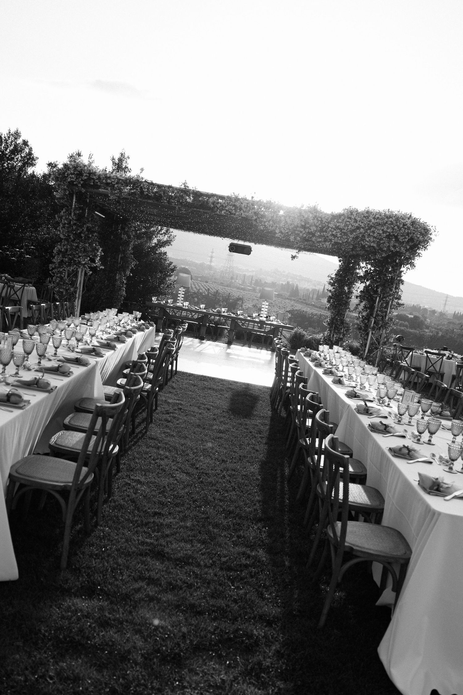 Black and white photo of an outdoor wedding reception setup with two long tables arranged in parallel on a lawn.