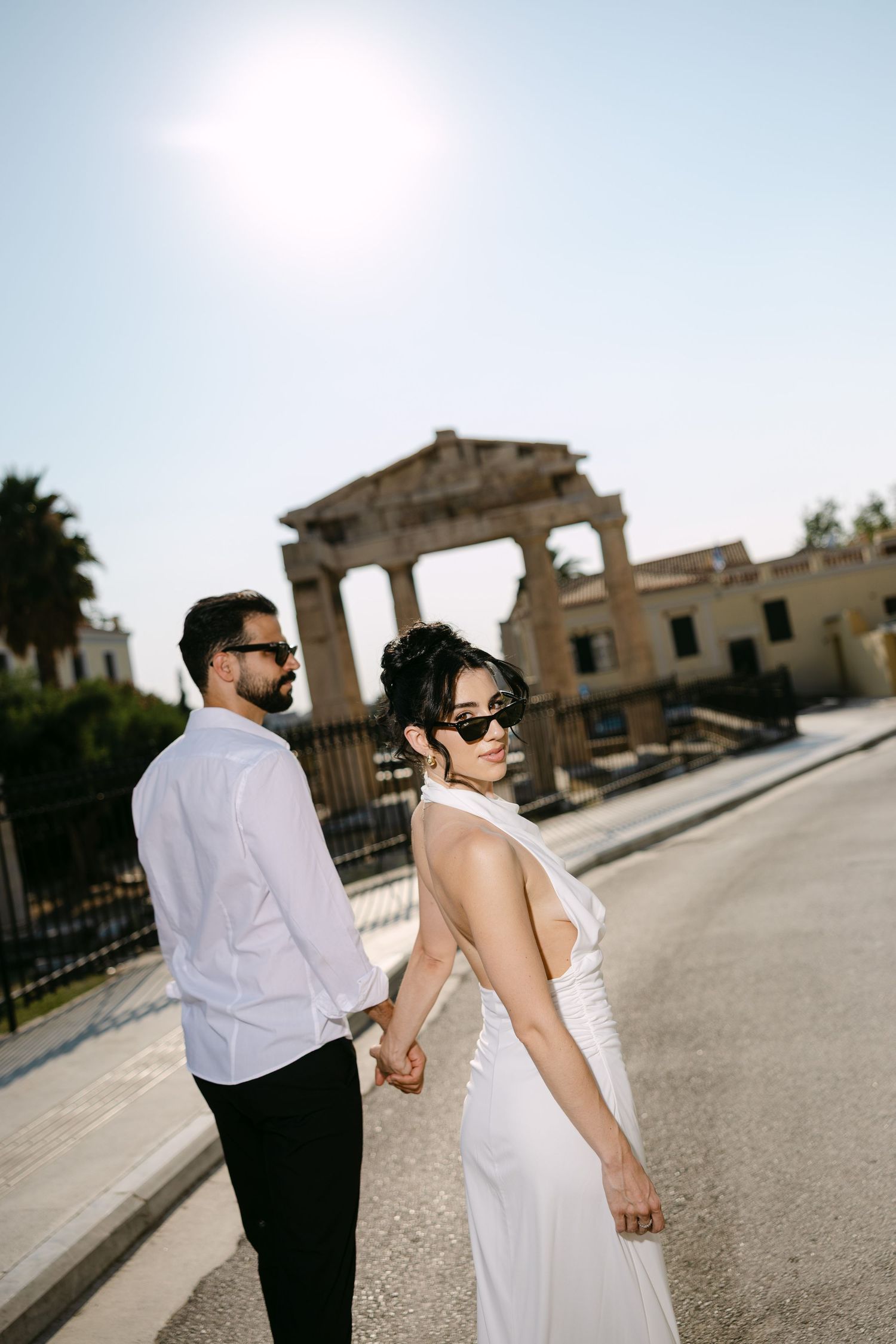 A couple walks together on a paved path with ancient Roman ruins visible in the background.