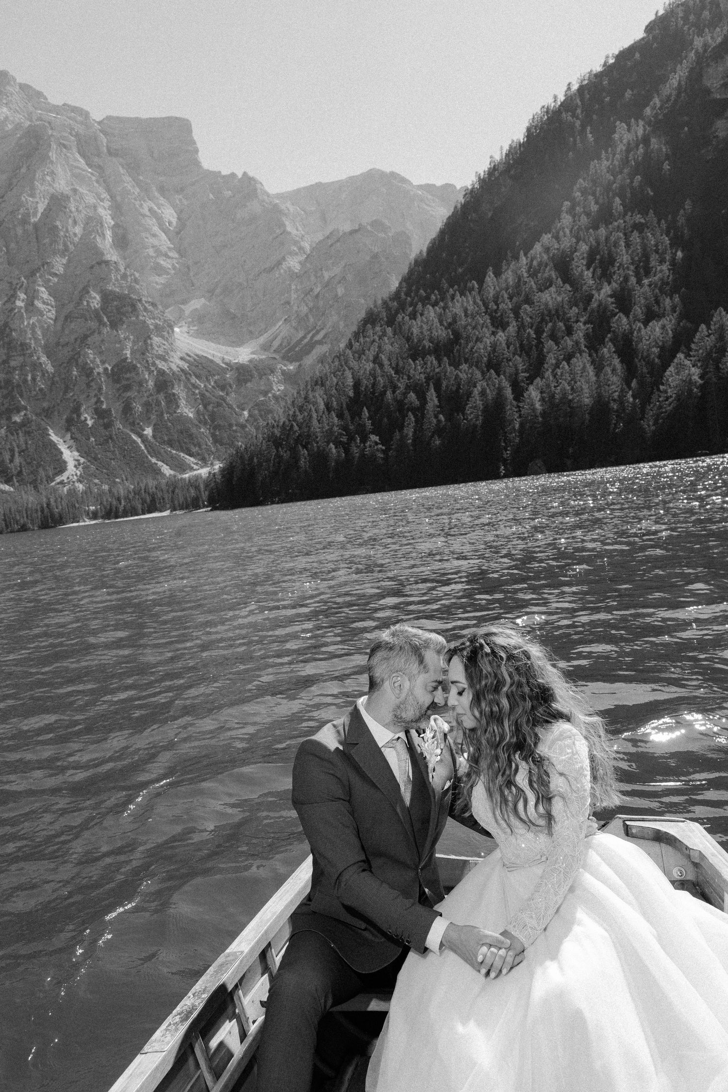 Romantic couple embraces on a boat with dramatic mountain lake scenery in the background.