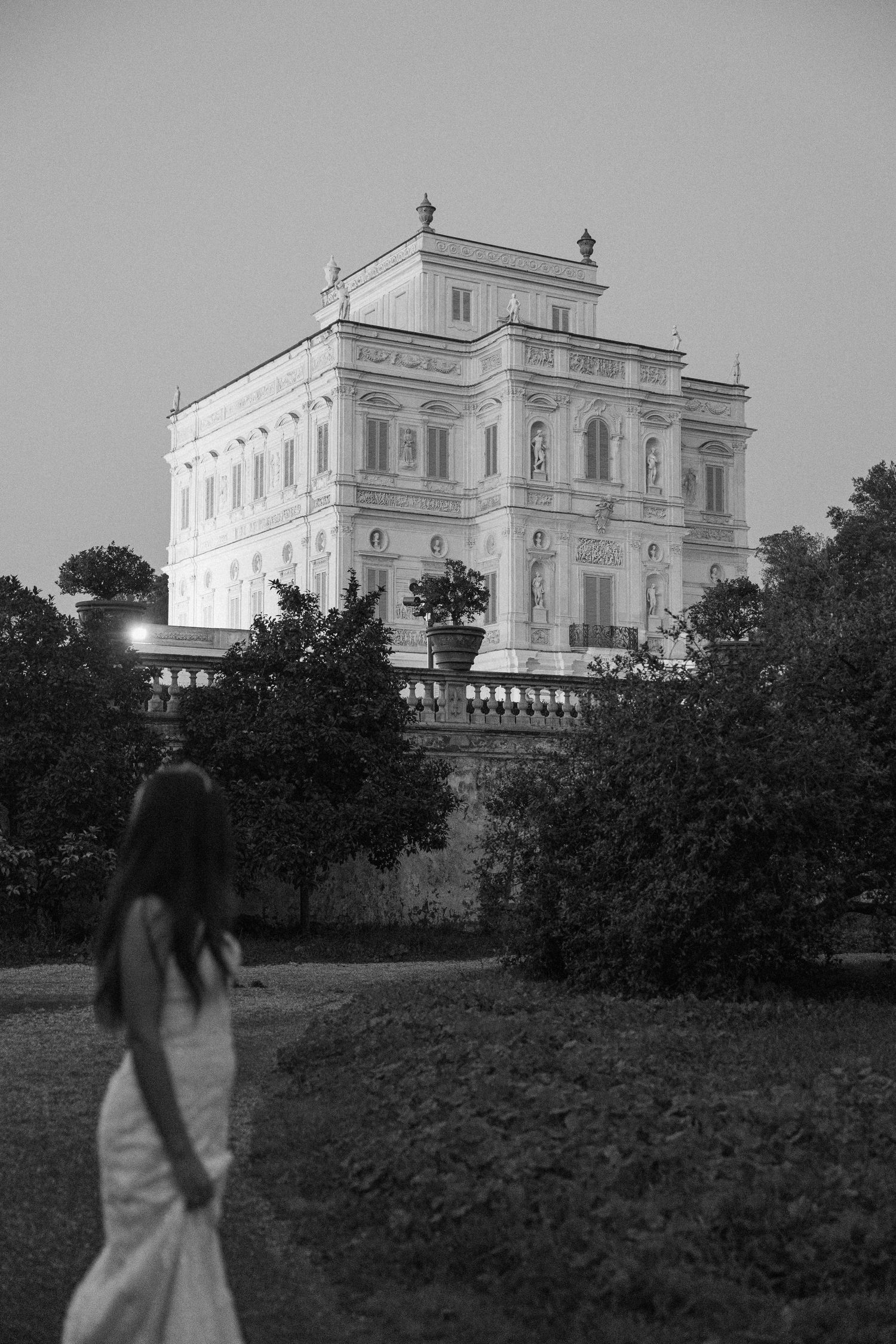 A white neoclassical villa stands elegantly among trees and gardens in this black and white photograph.
