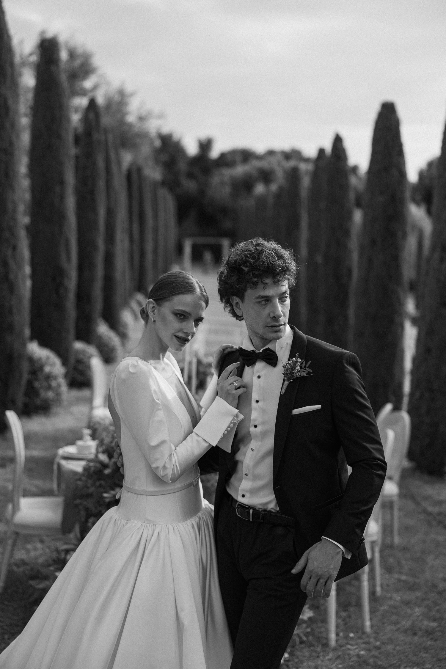 A romantic black and white wedding photoshoot in a cypress tree-lined path shows intimate moments between newlyweds.