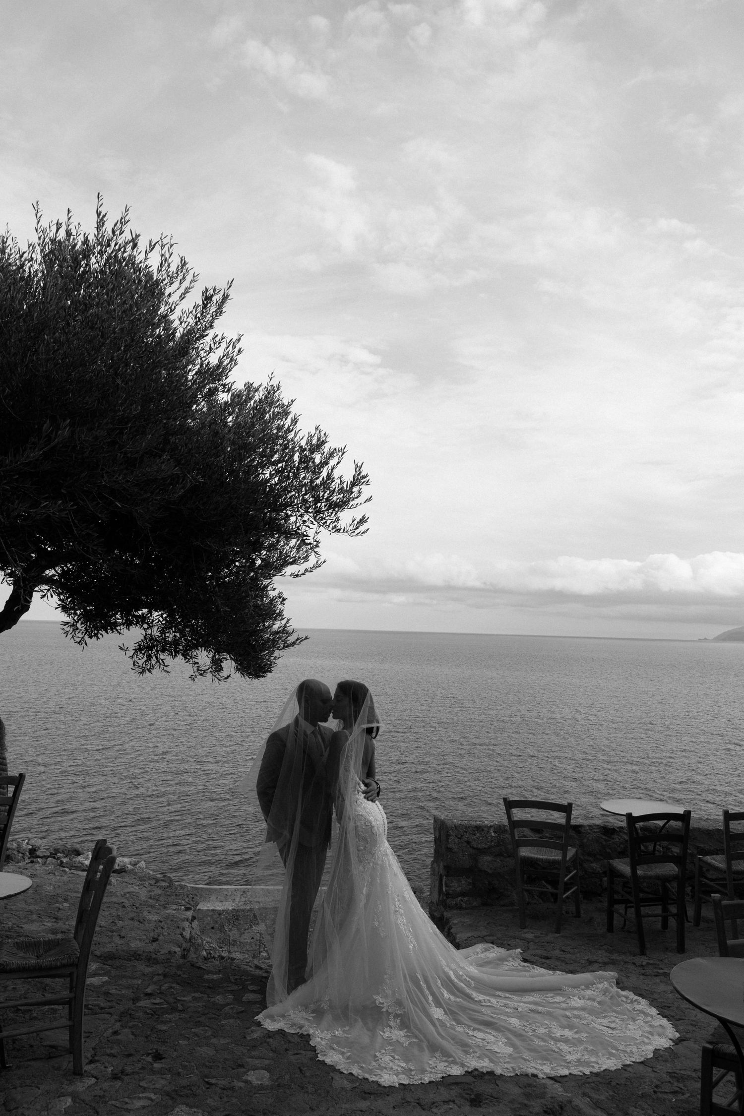 Black and white panoramic sequence of a couple in wedding attire posing by the sea against a cloudy Mediterranean sky.