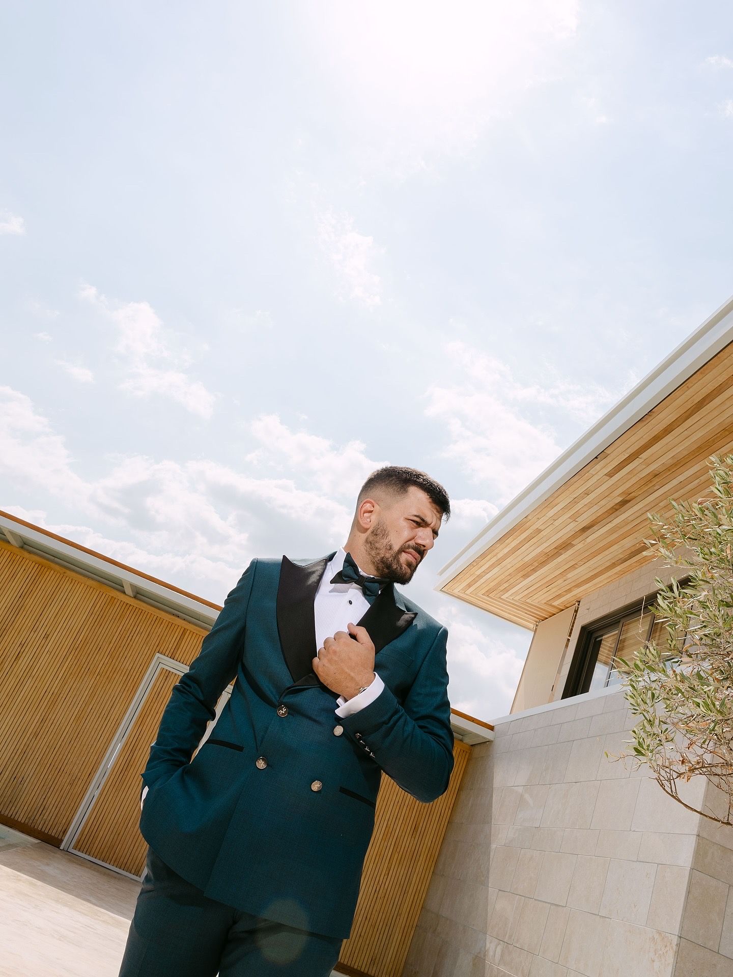 A person in a dark suit adjusts their tie while standing against a modern architectural backdrop.