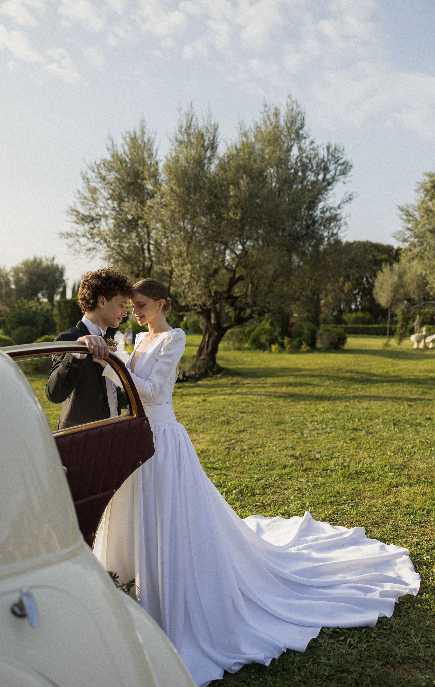 A flowing white wedding dress train sweeps across an olive grove field during a golden hour photoshoot.