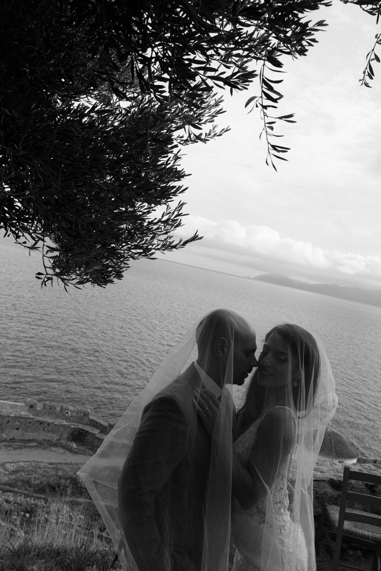 A romantic silhouette of a couple kissing against a scenic ocean backdrop with trees framing the shot.