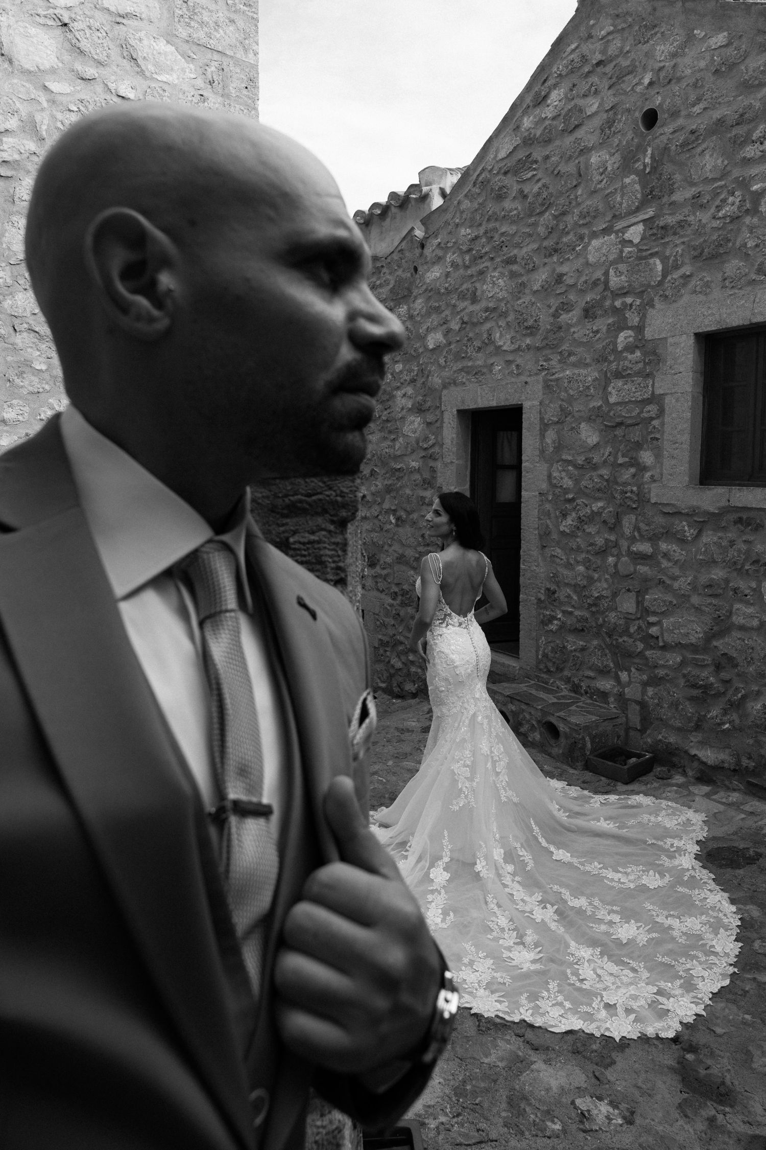 Black and white wedding photos show emotional reactions and a bride in a flowing dress with cathedral train against stone walls.