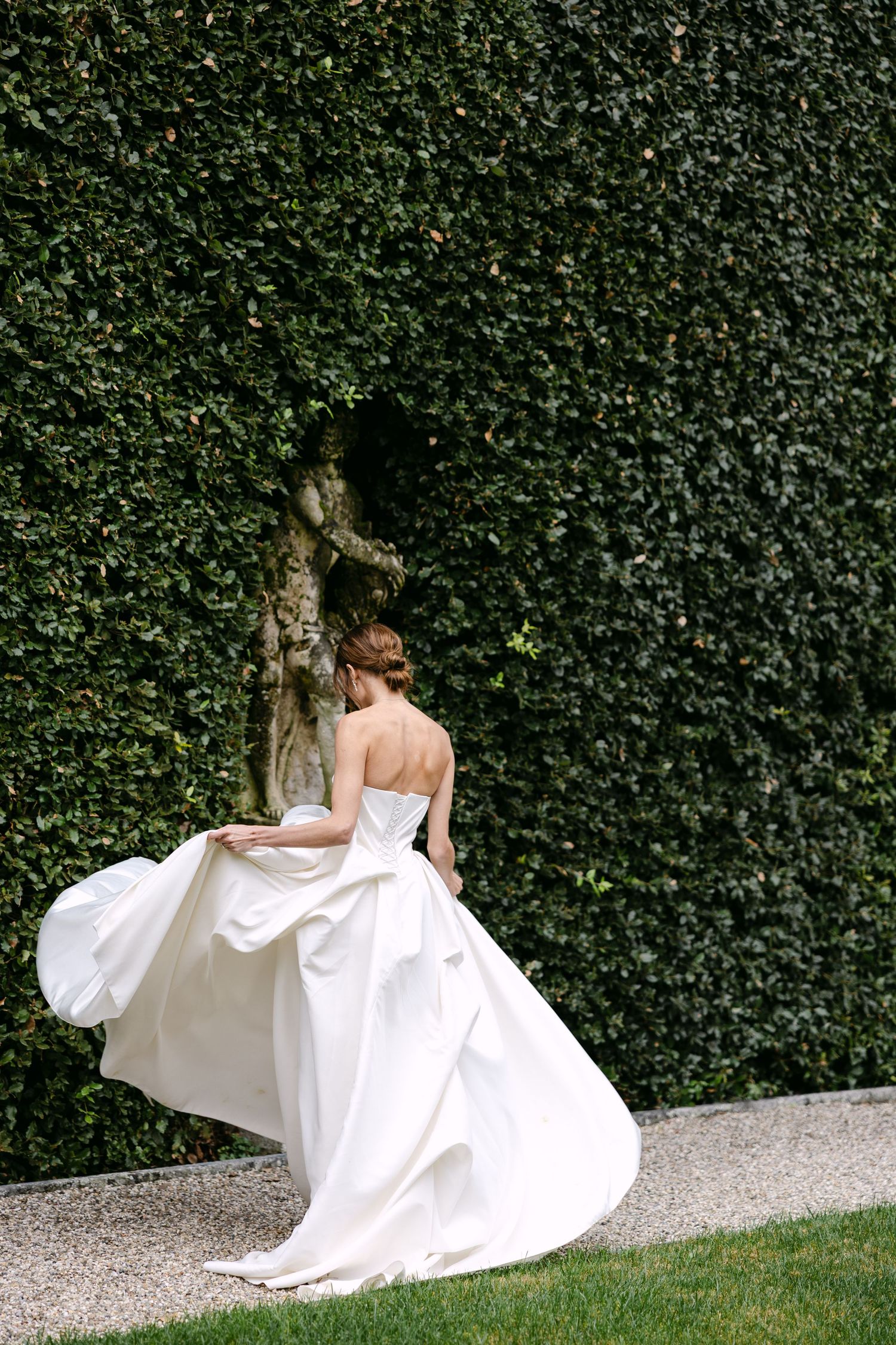 White wedding dress flowing in the breeze against a lush ivy-covered wall backdrop.