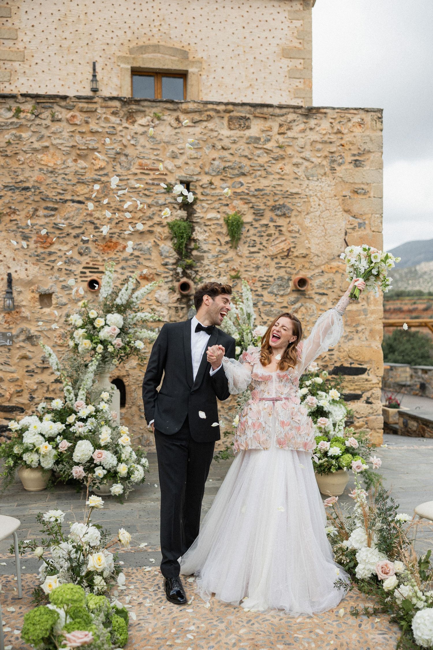 Joyful couple shares candid moments against stone castle walls adorned with elegant white floral arrangements.