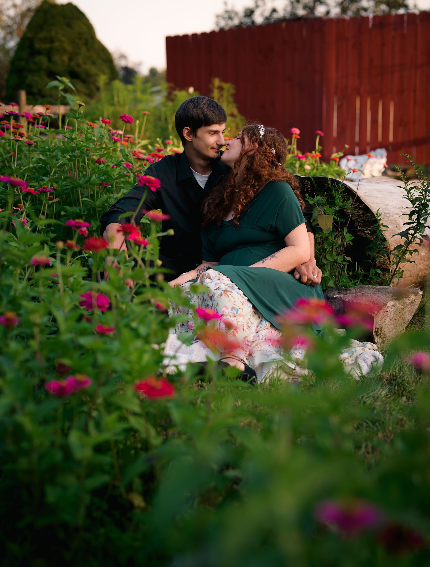 Couple shares a kiss surrounded by colorful blooming flowers in a lush garden setting.
