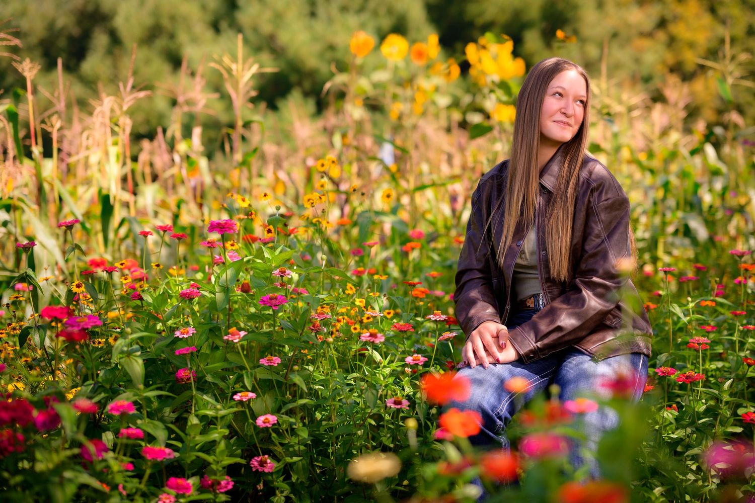 Woman with long hair sitting peacefully among colorful wildflowers and tall plants in a lush garden.