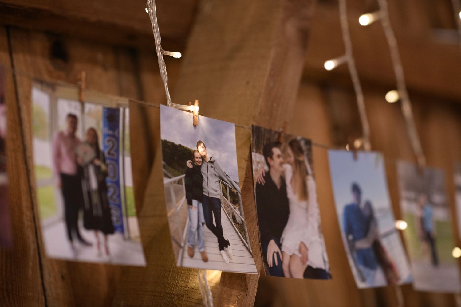 Wedding photos displayed on string lights with wooden clothespins in rustic barn decoration.