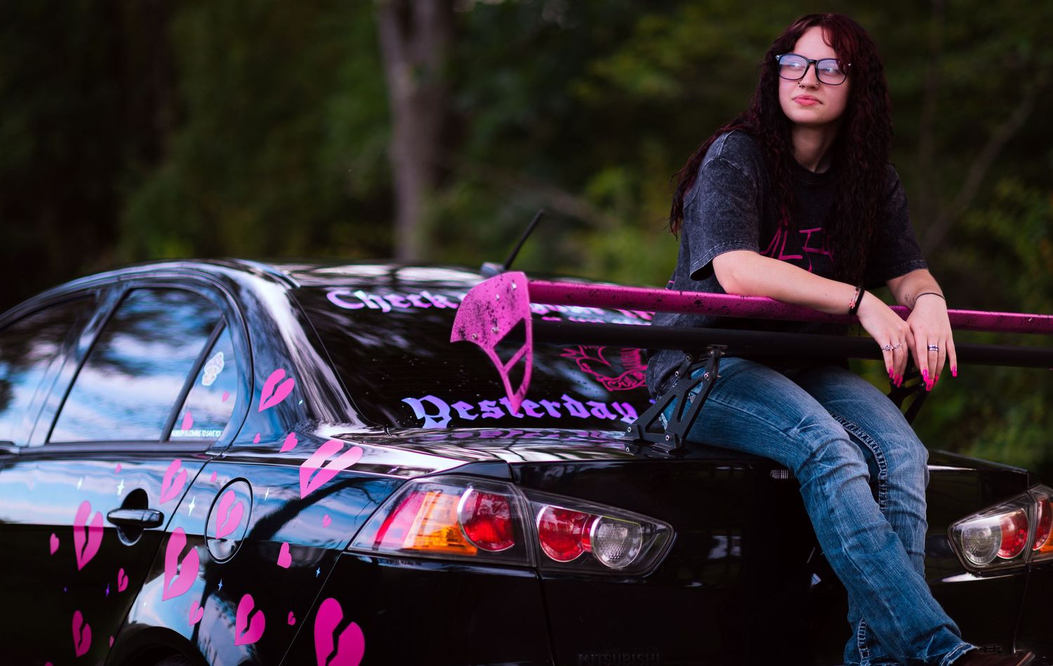 Person leaning on a custom black and pink car with artistic graphics outdoors.