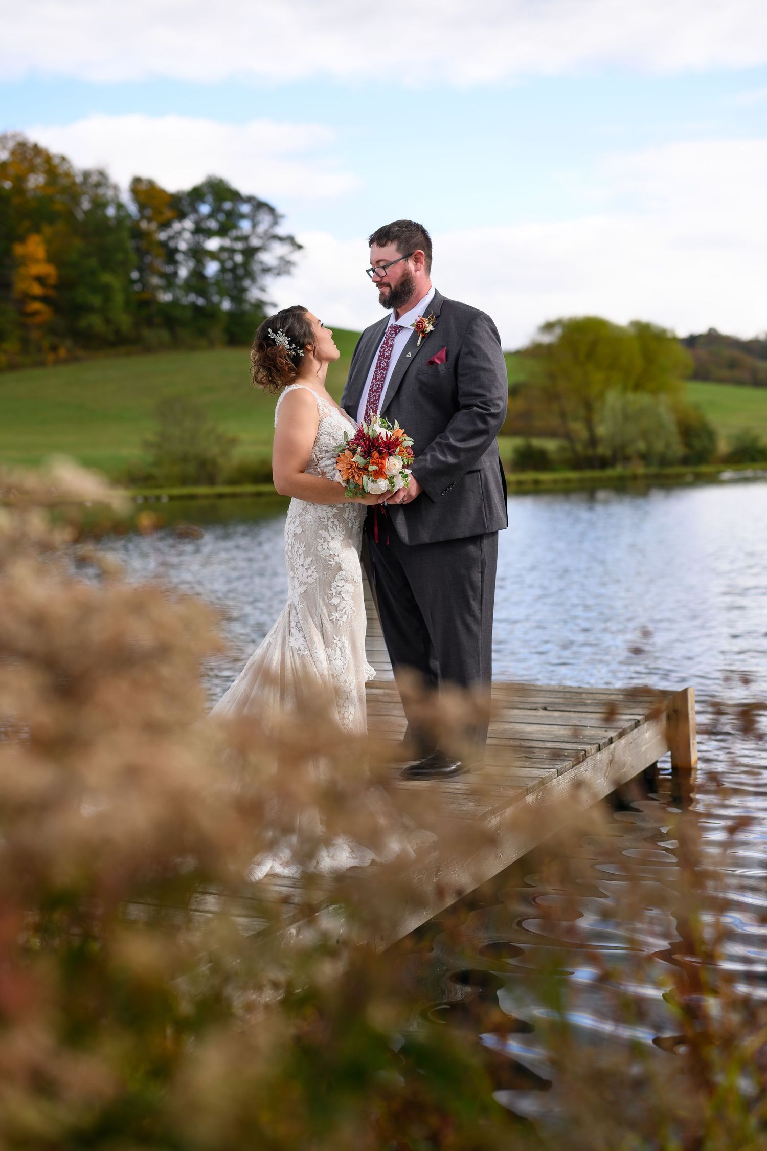 Bride and groom share a romantic moment on a wooden dock by a lake during a fall wedding.
