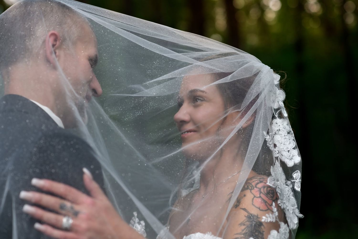 Romantic bride and groom sharing an intimate moment under a lace wedding veil in the forest.