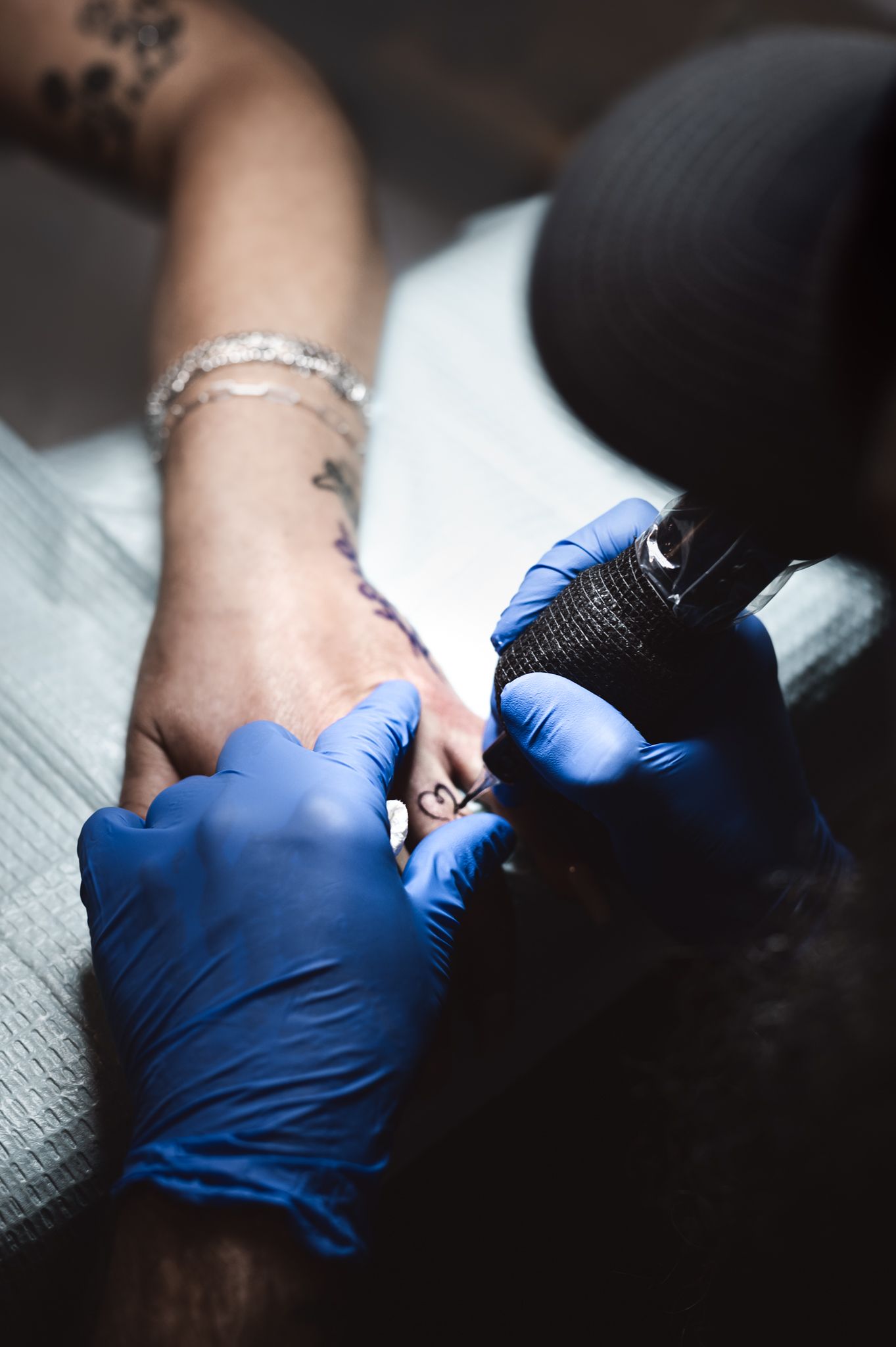 Tattoo artist wearing blue gloves carefully tattooing a clients wrist with a tattoo machine in a studio.