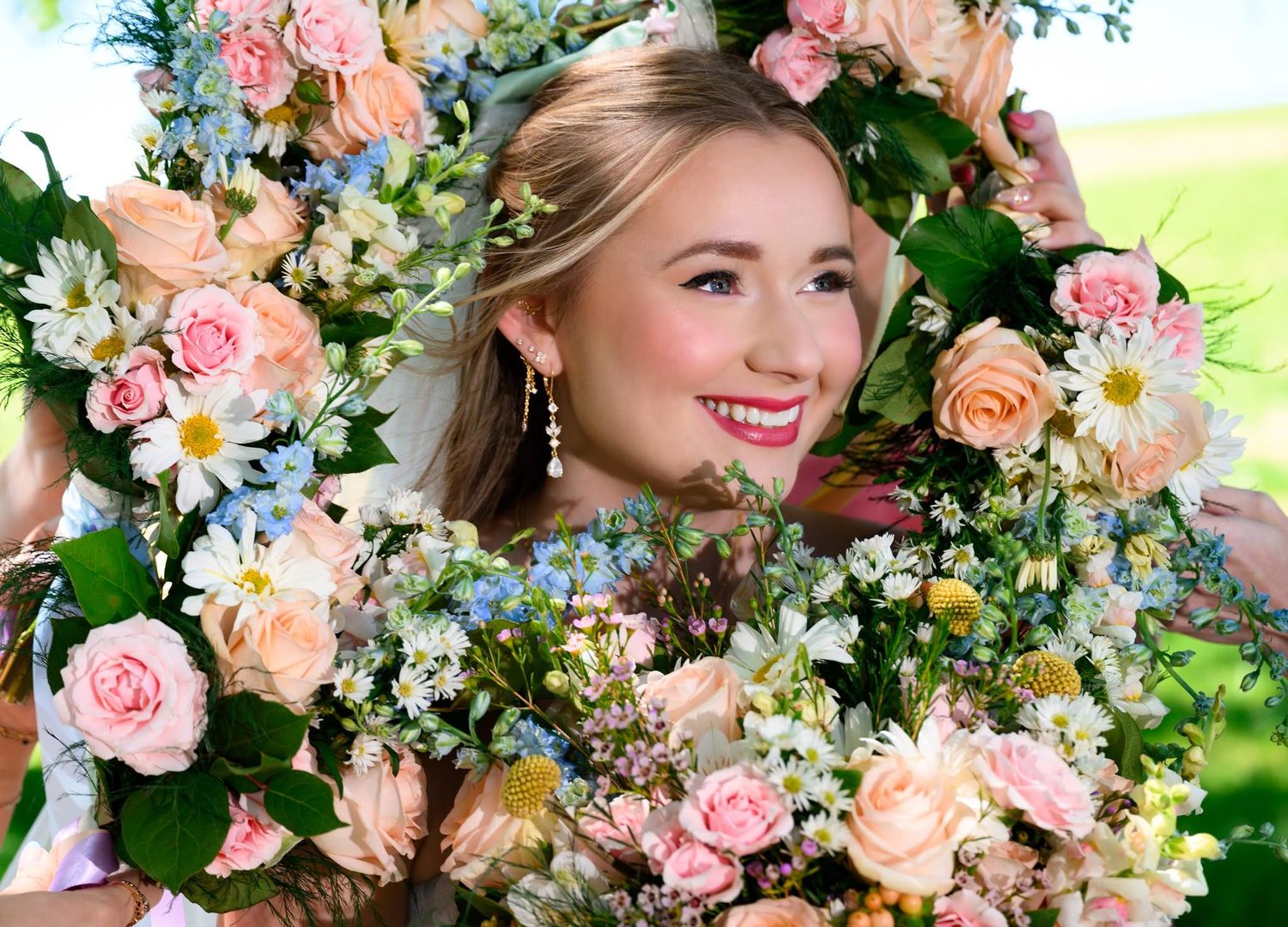 Young bride smiling surrounded by a beautiful wreath of pink roses, daisies, and pastel spring flowers.