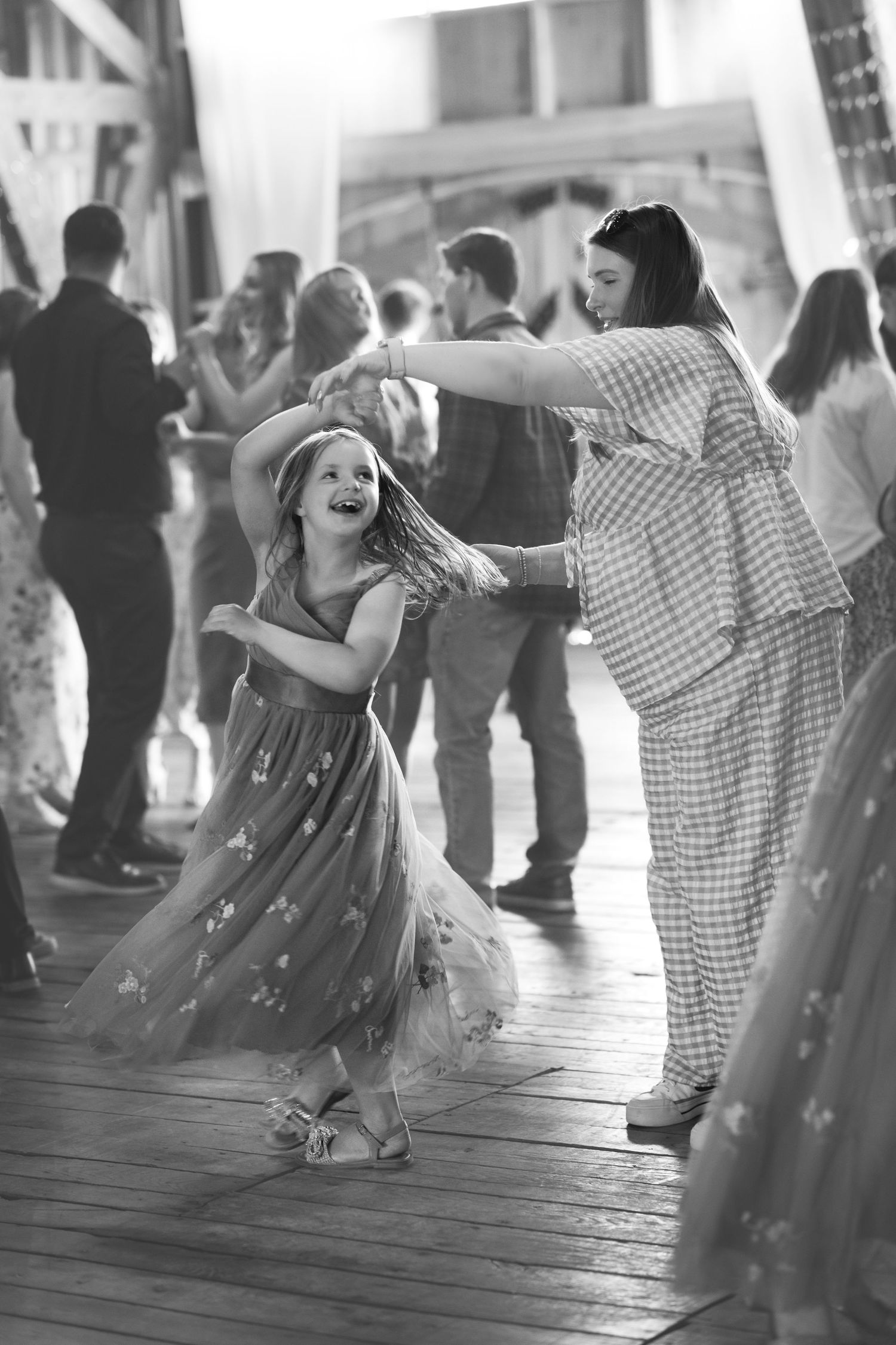 Black and white photo of a woman and young girl dancing joyfully together at an indoor event or celebration.