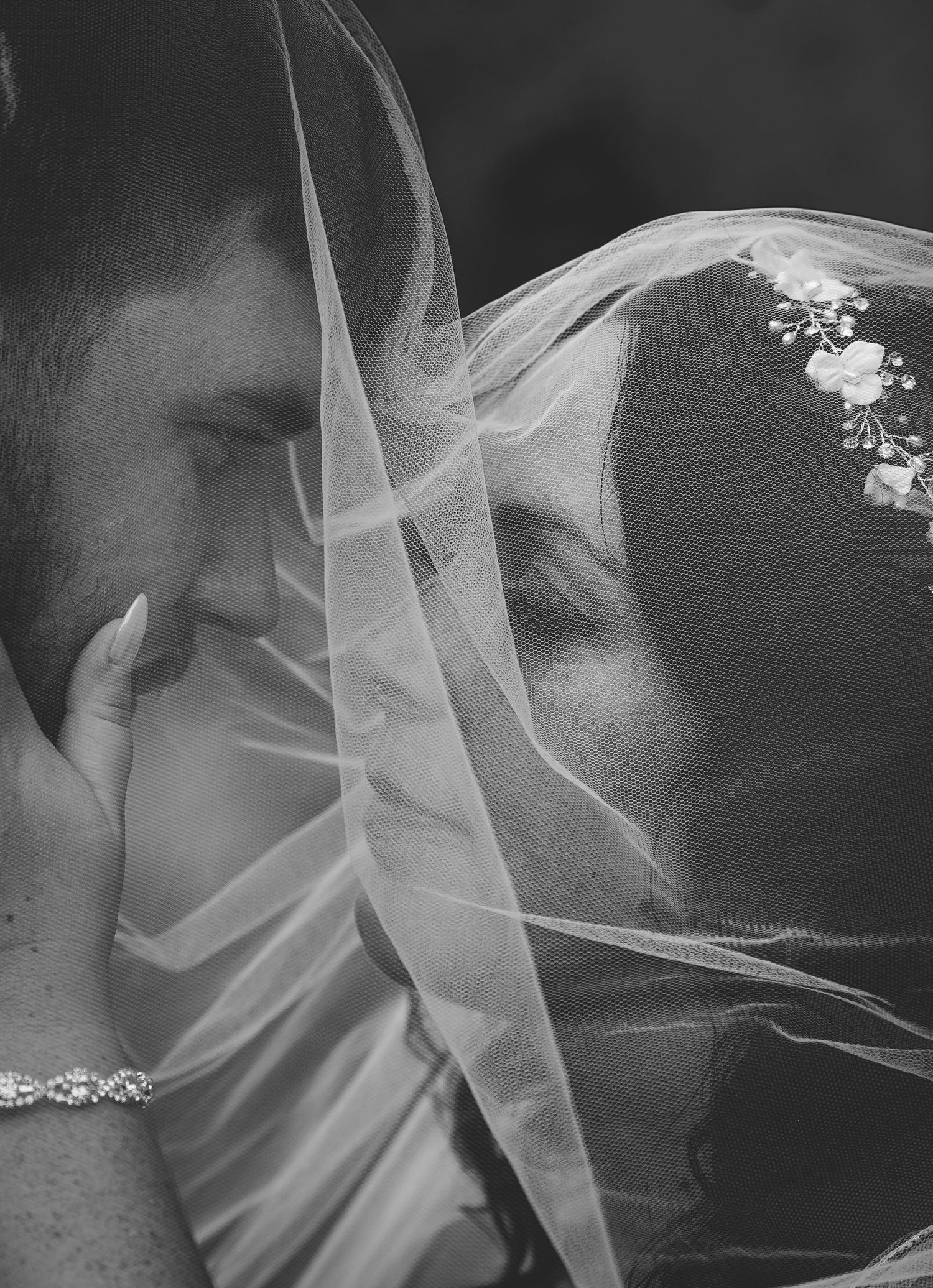 Romantic black and white photo of bride and groom sharing intimate moment under wedding veil.