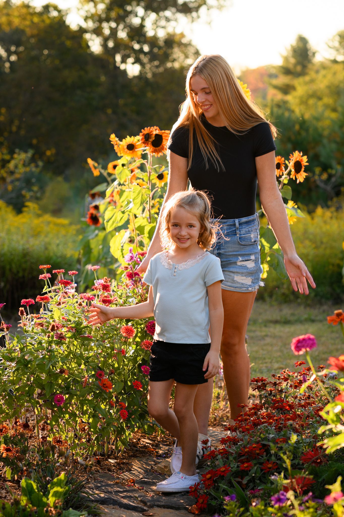 Mother and daughter walking through a vibrant sunflower garden at golden hour sunset.