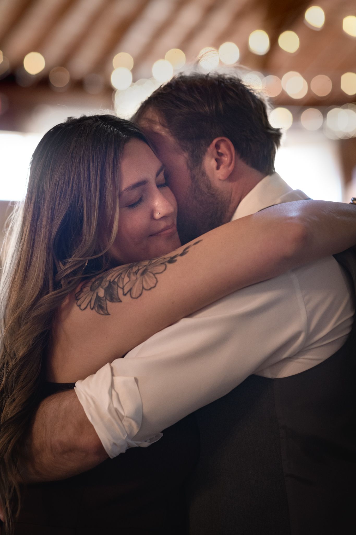 Bride with floral tattoo and groom share a tender embrace during their first dance at reception.