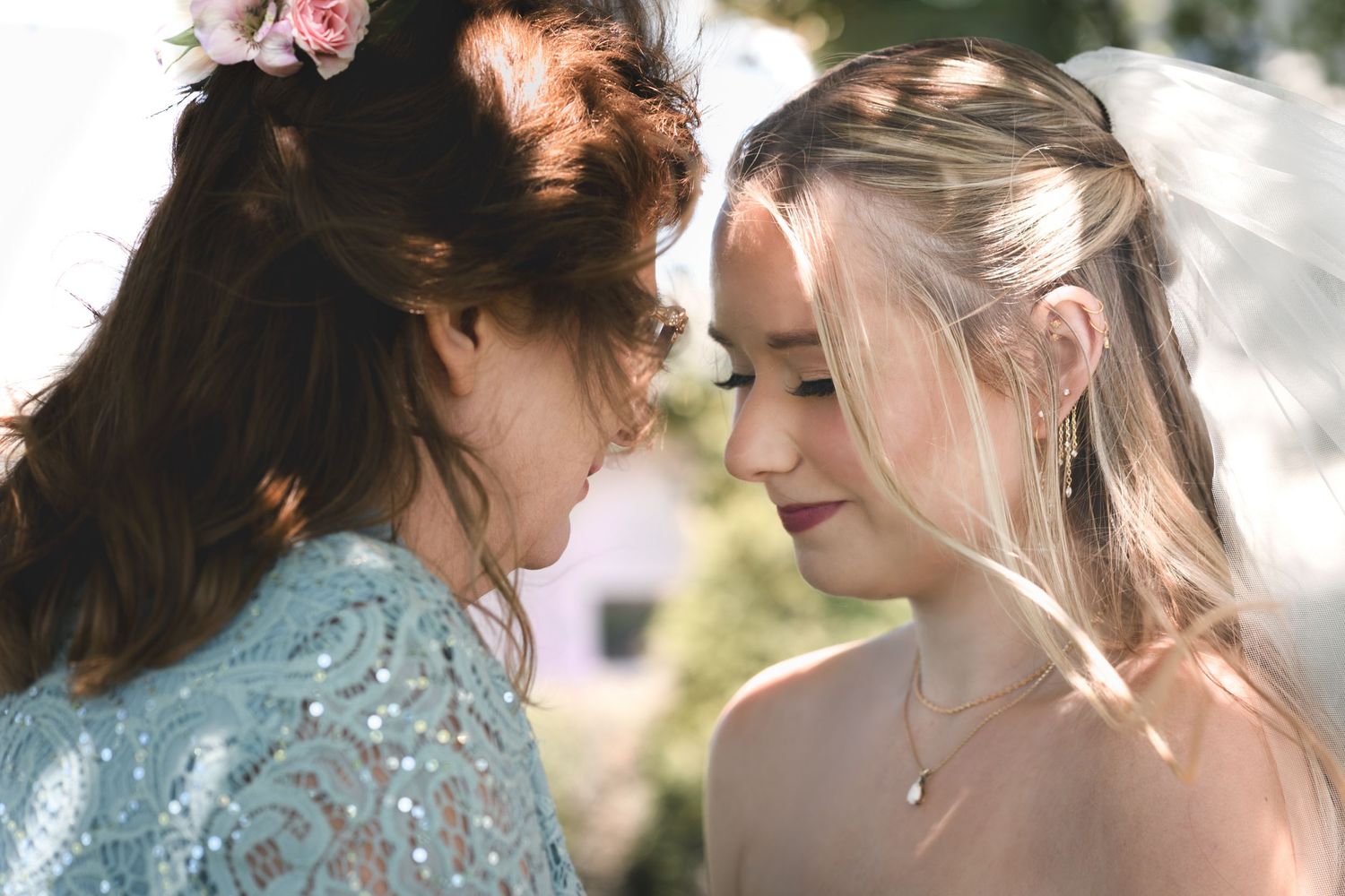 Two brides share an intimate moment, one in blue lace and one in white, with floral hair accessories outdoors.