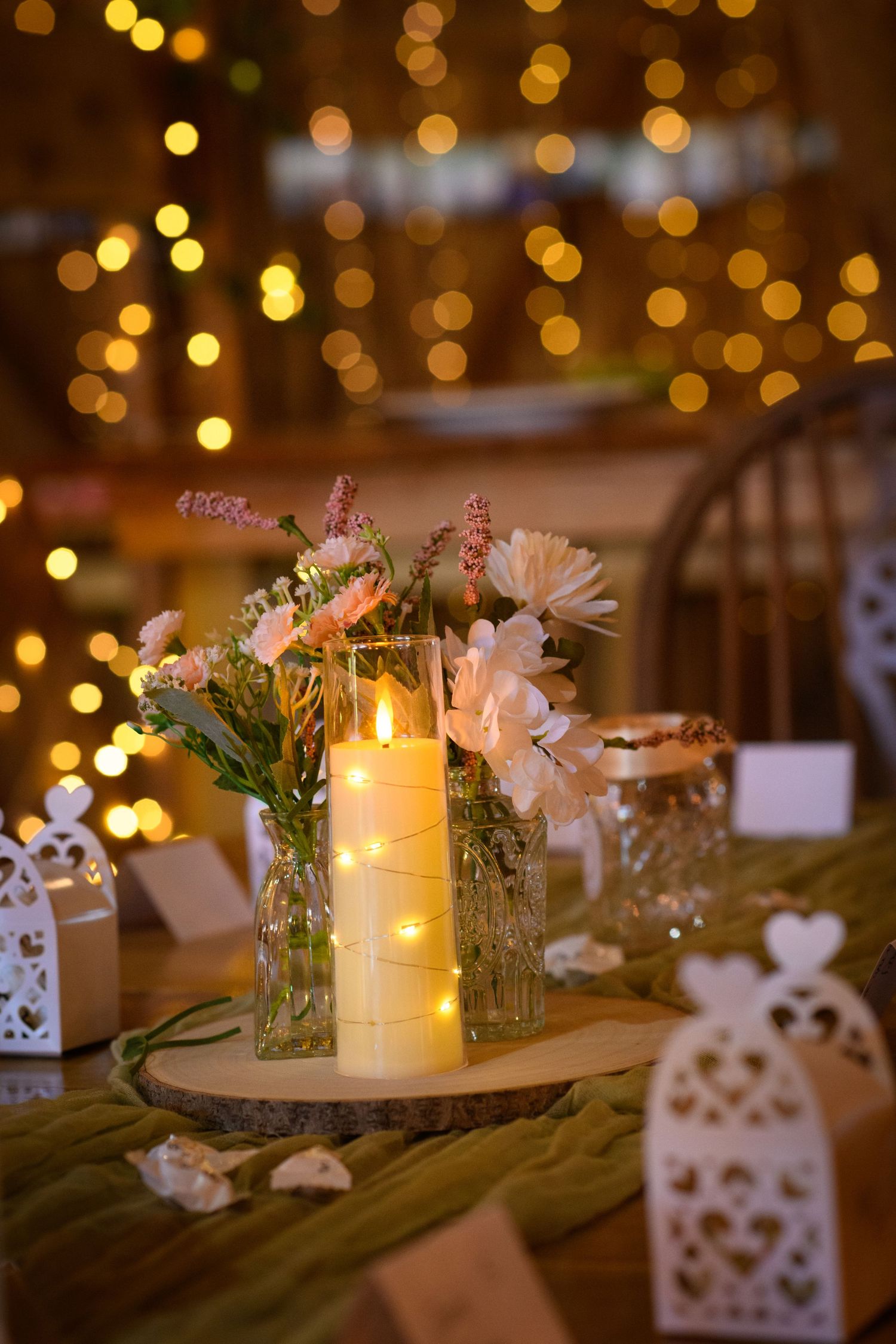 Elegant rustic wedding table centerpiece with glowing candle, wildflowers, and warm bokeh lights.