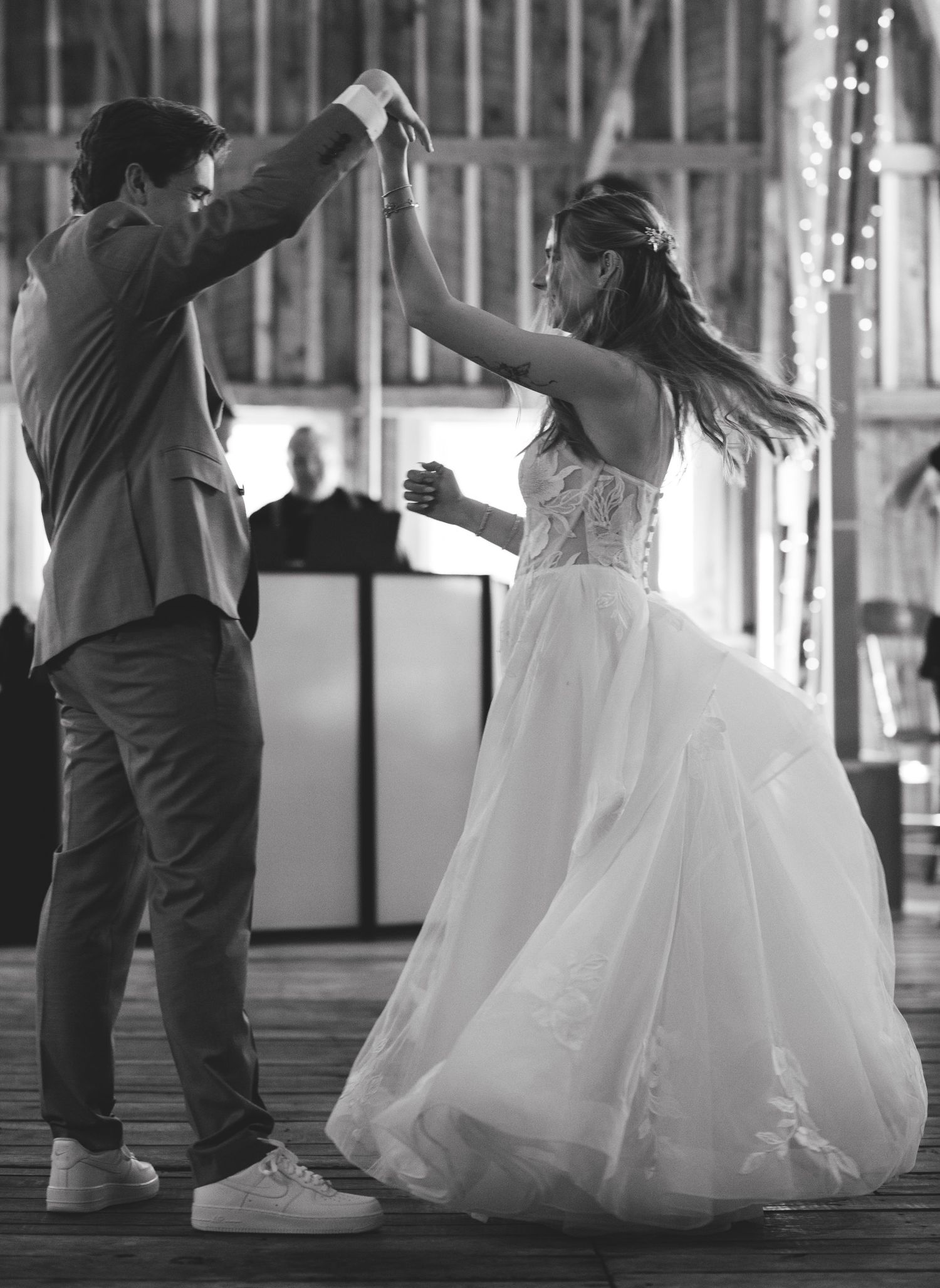 Black and white photo of bride and groom sharing first dance in rustic barn venue with fairy lights.