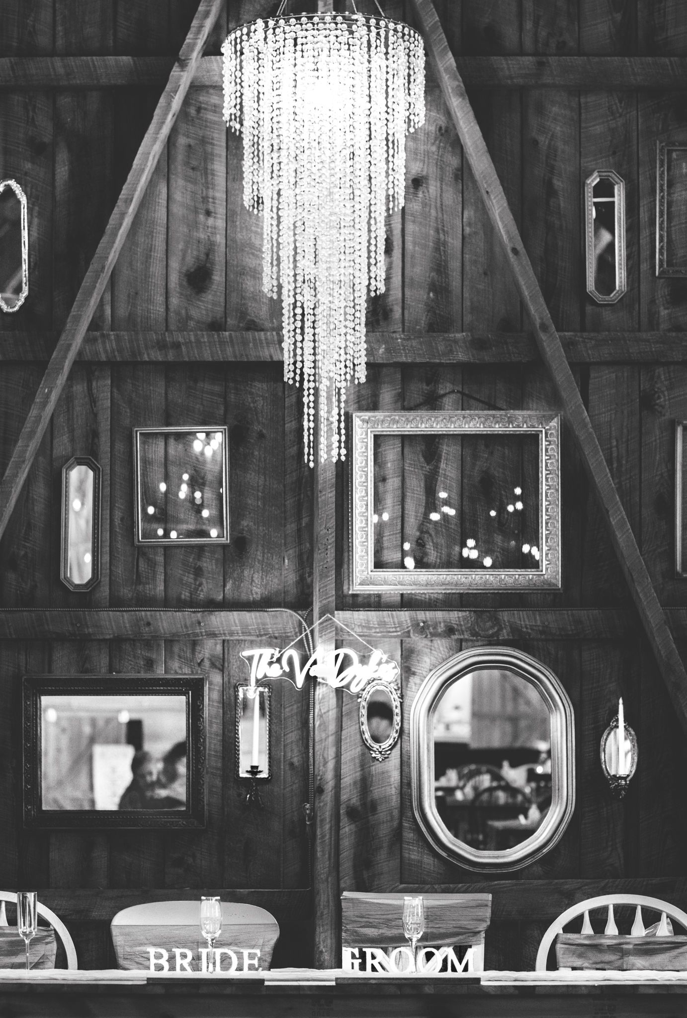 Black and white photo of rustic barn wedding venue interior with crystal chandelier and bride groom signs.