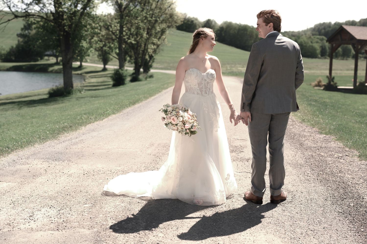 Bride and groom walking hand in hand down a gravel path on their wedding day at an outdoor venue.