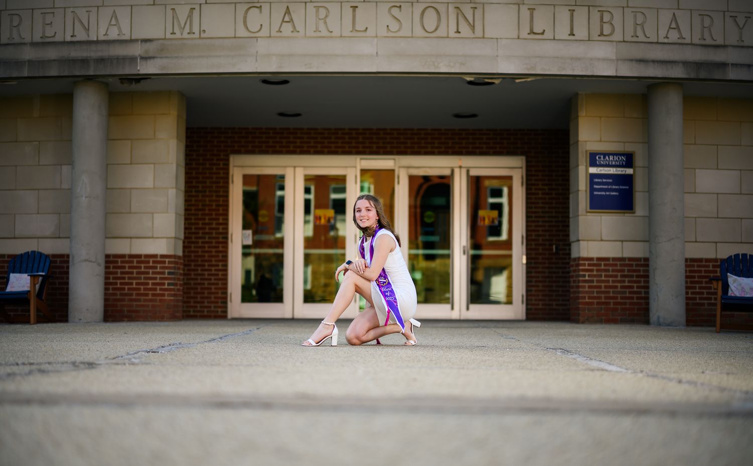A young woman in a pageant gown and crown poses gracefully outside the Carlson Library entrance.