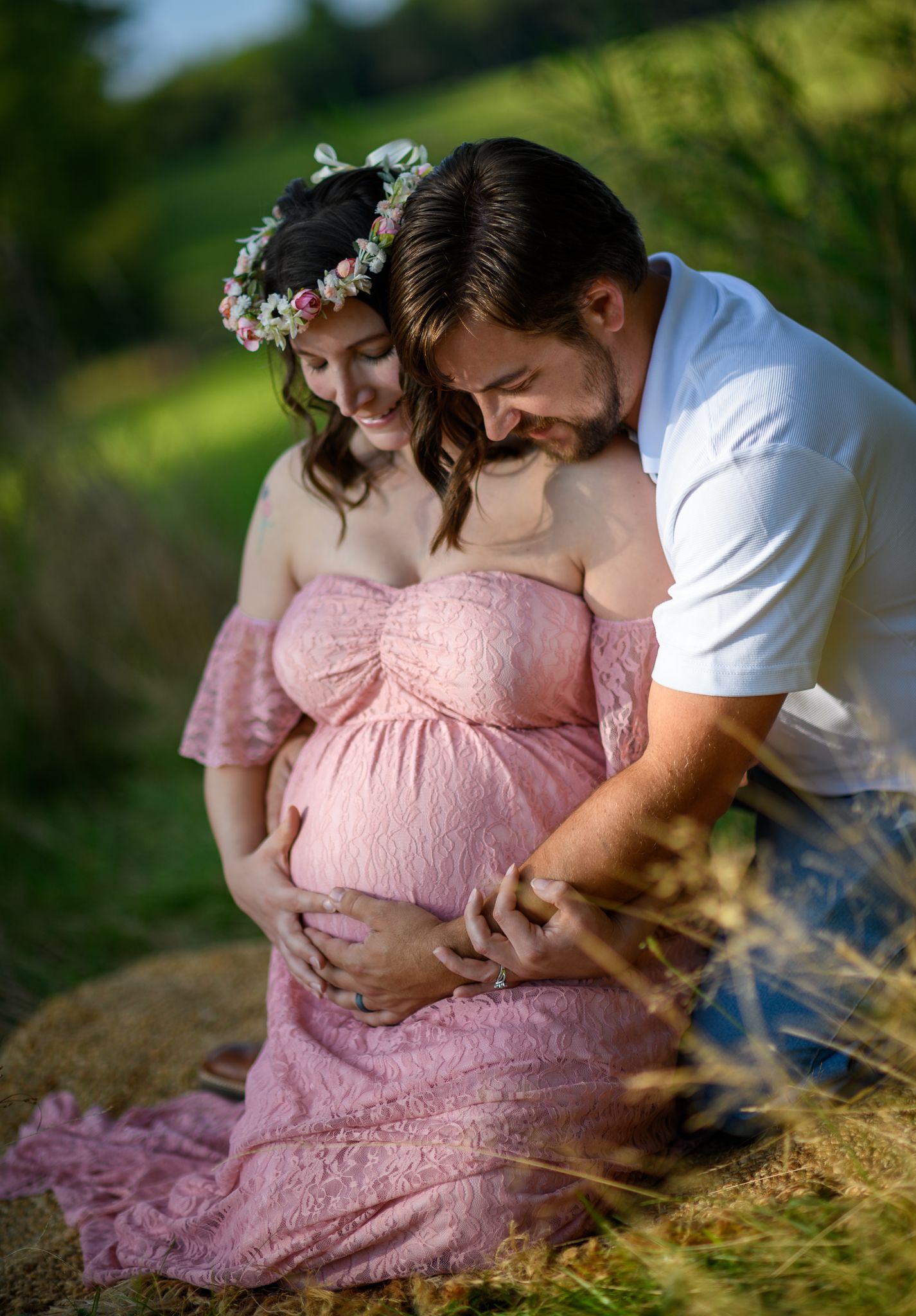 Couple tenderly cradling pregnant belly during outdoor maternity photo session in golden light.