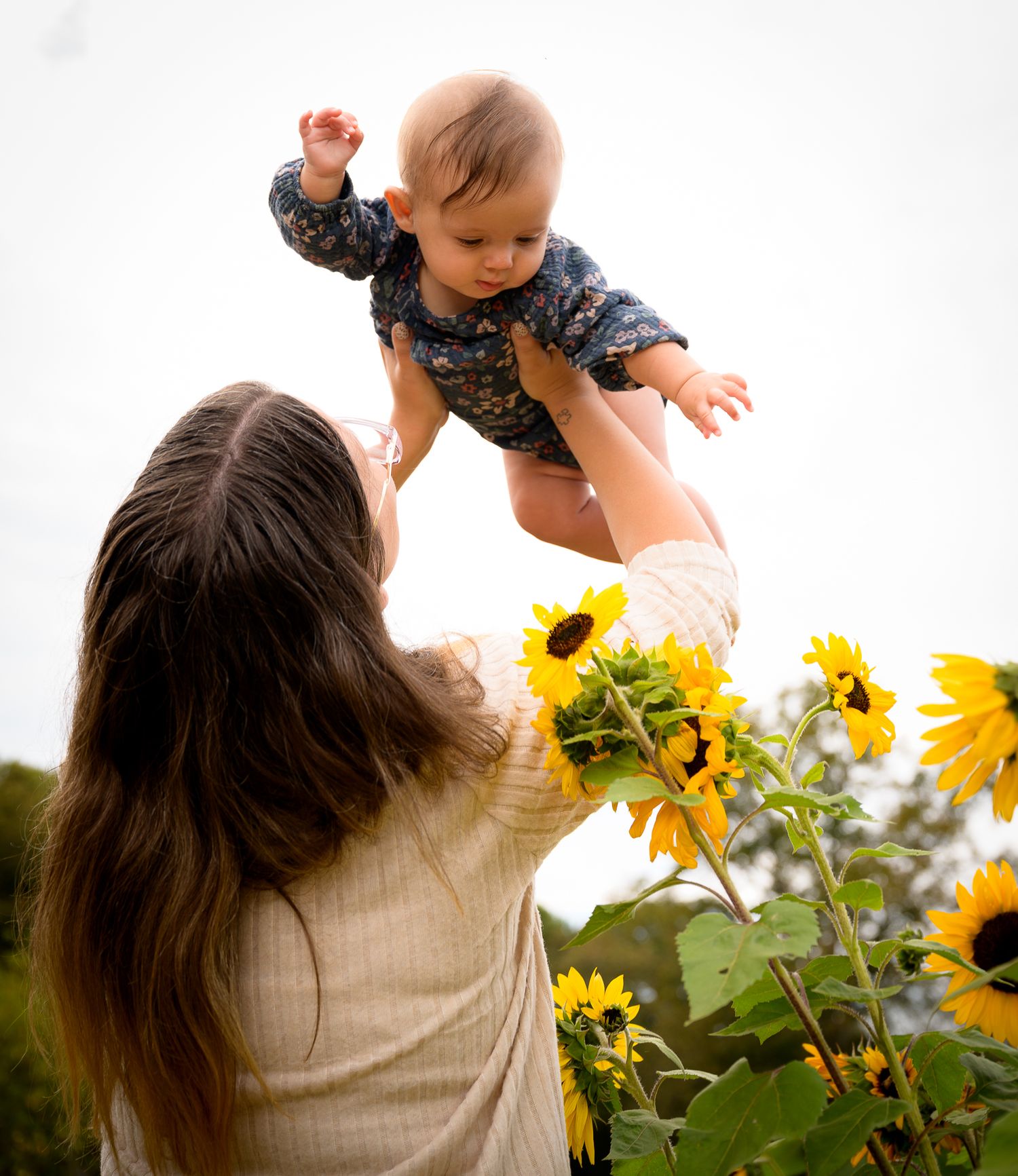 Mother lifting baby in sunflower field outdoors.
