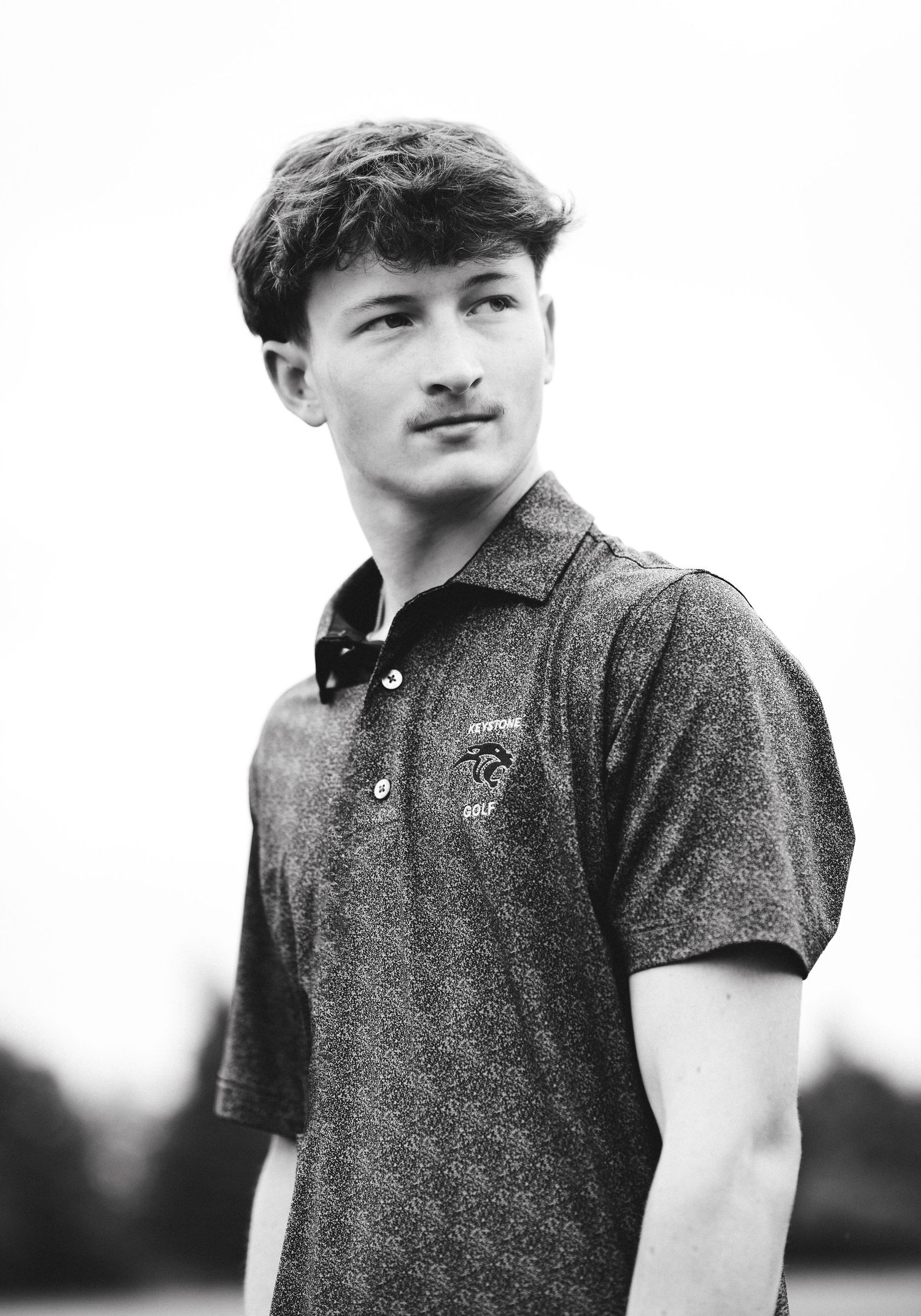 Black and white portrait of a young man in a golf polo shirt posing outdoors.