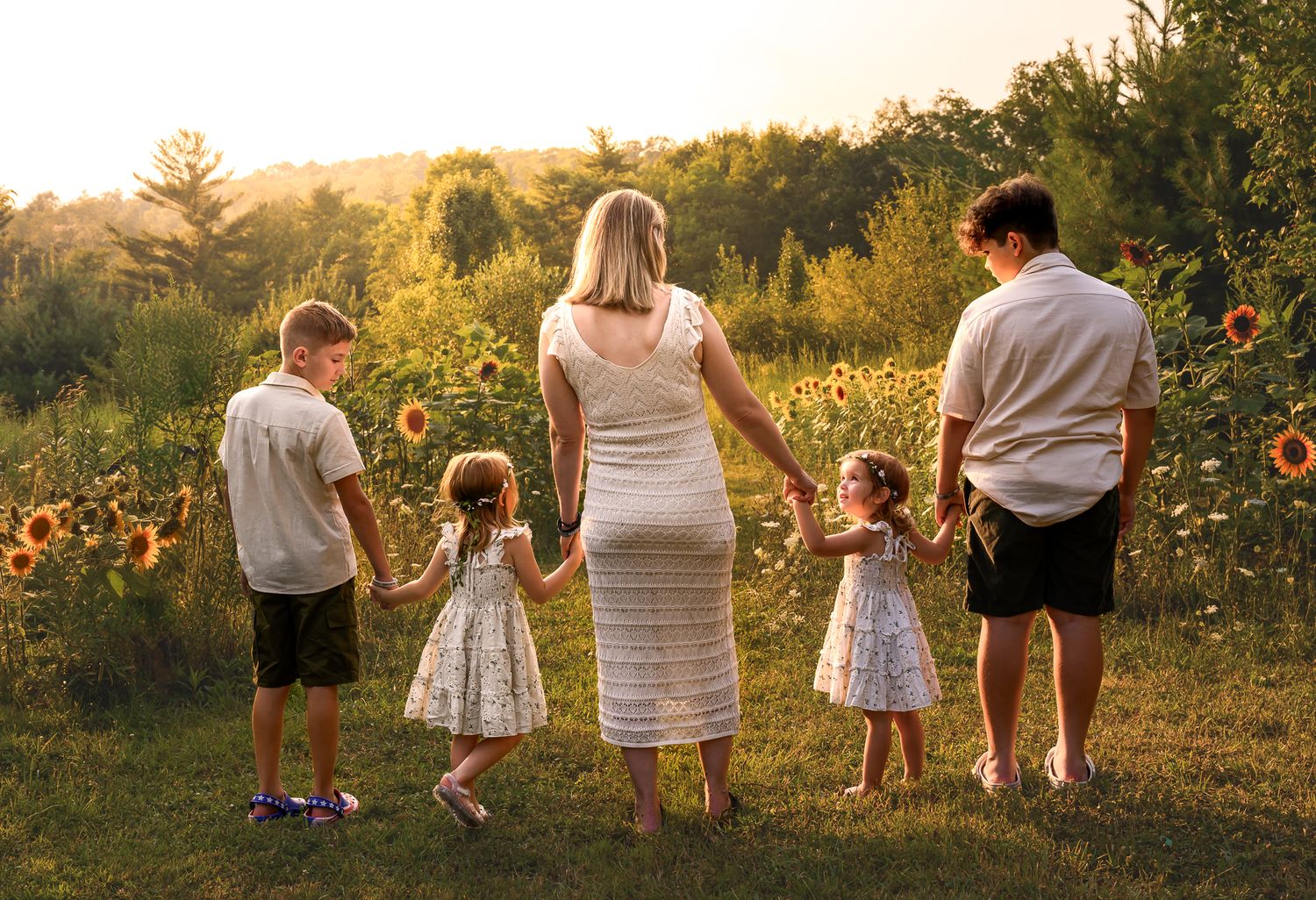 A family of five holds hands in a sunflower field during a golden hour outdoor photo session.