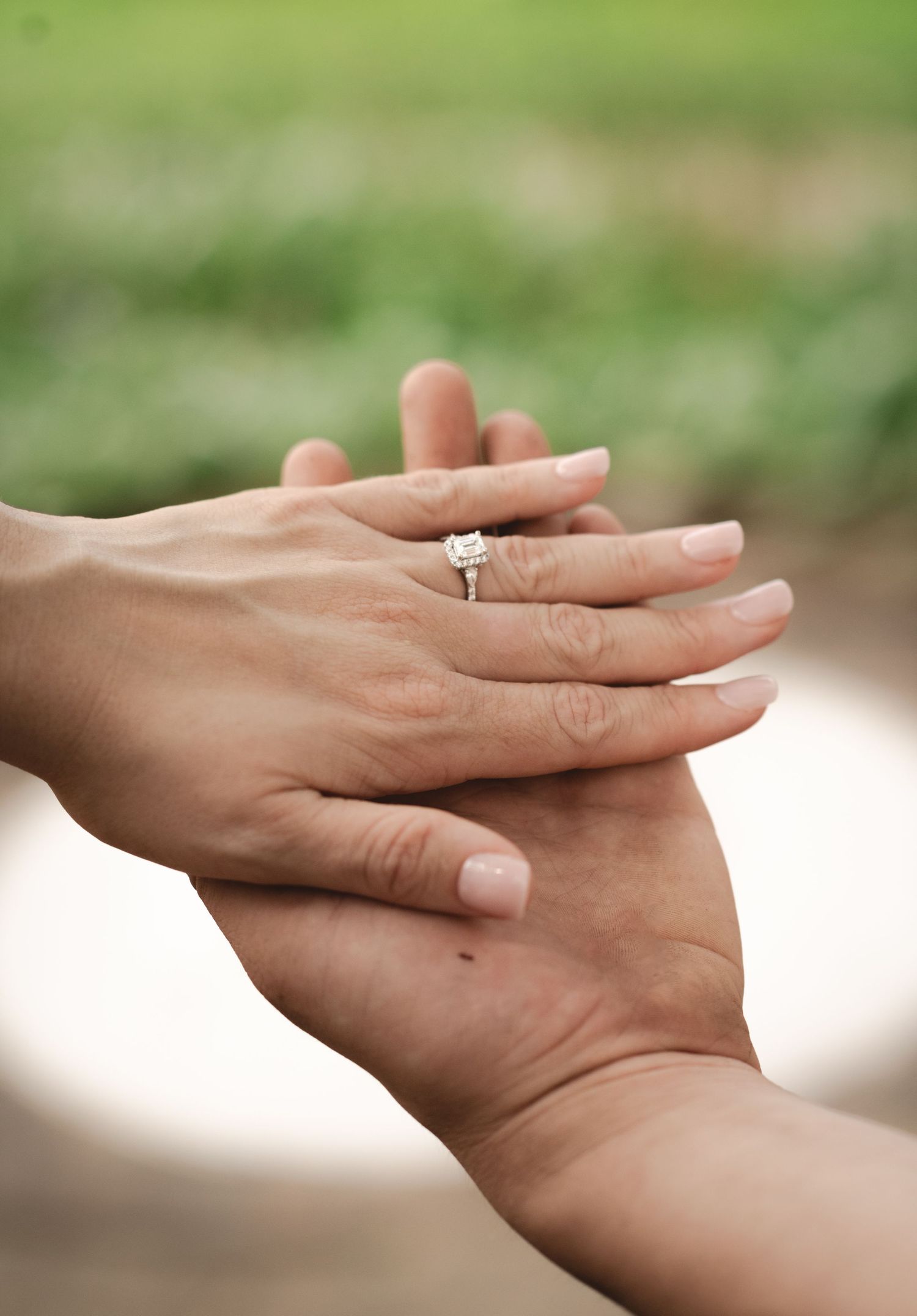 Close-up of two hands holding, with a sparkling diamond engagement ring on the woman's finger.
