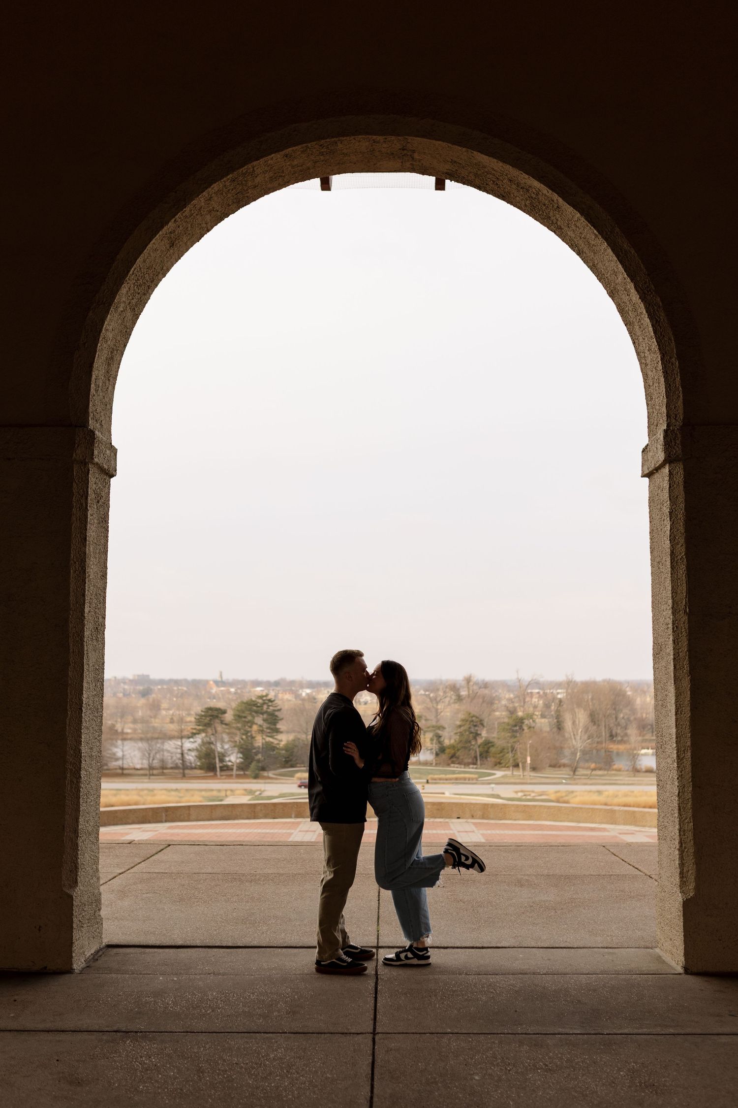 Silhouette of a couple kissing under a large stone archway with a scenic landscape visible in the background.