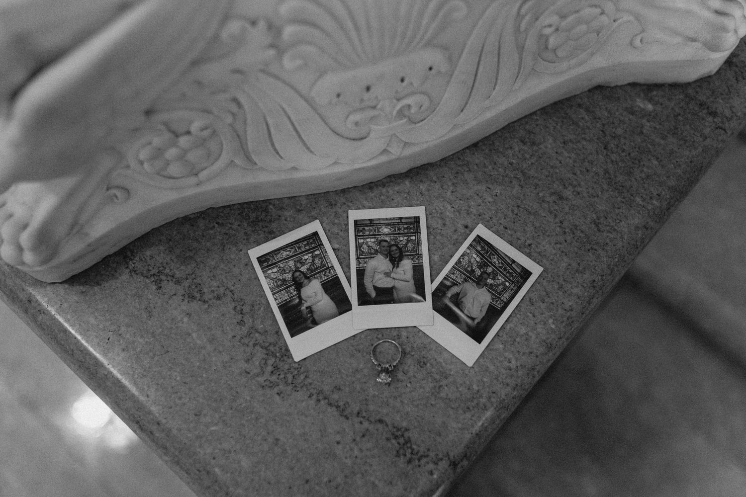 Black and white flat lay of three Polaroid photos and a ring on a stone surface.