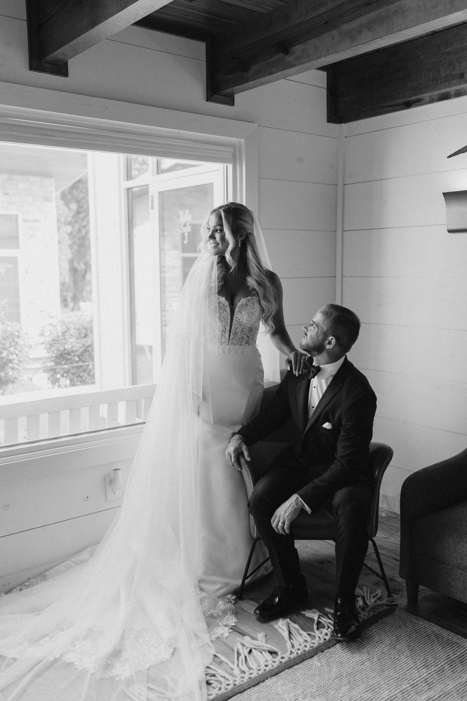 Bride and groom share a quiet moment by a window in a charming rustic room in black and white portrait.